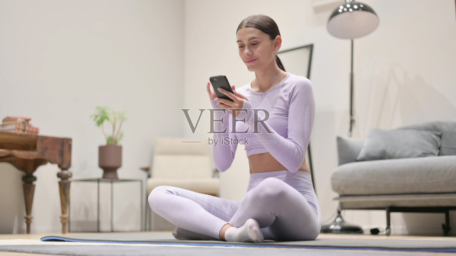 年轻的拉丁女子在家里的瑜伽垫上使用智能手机照片摄影图片