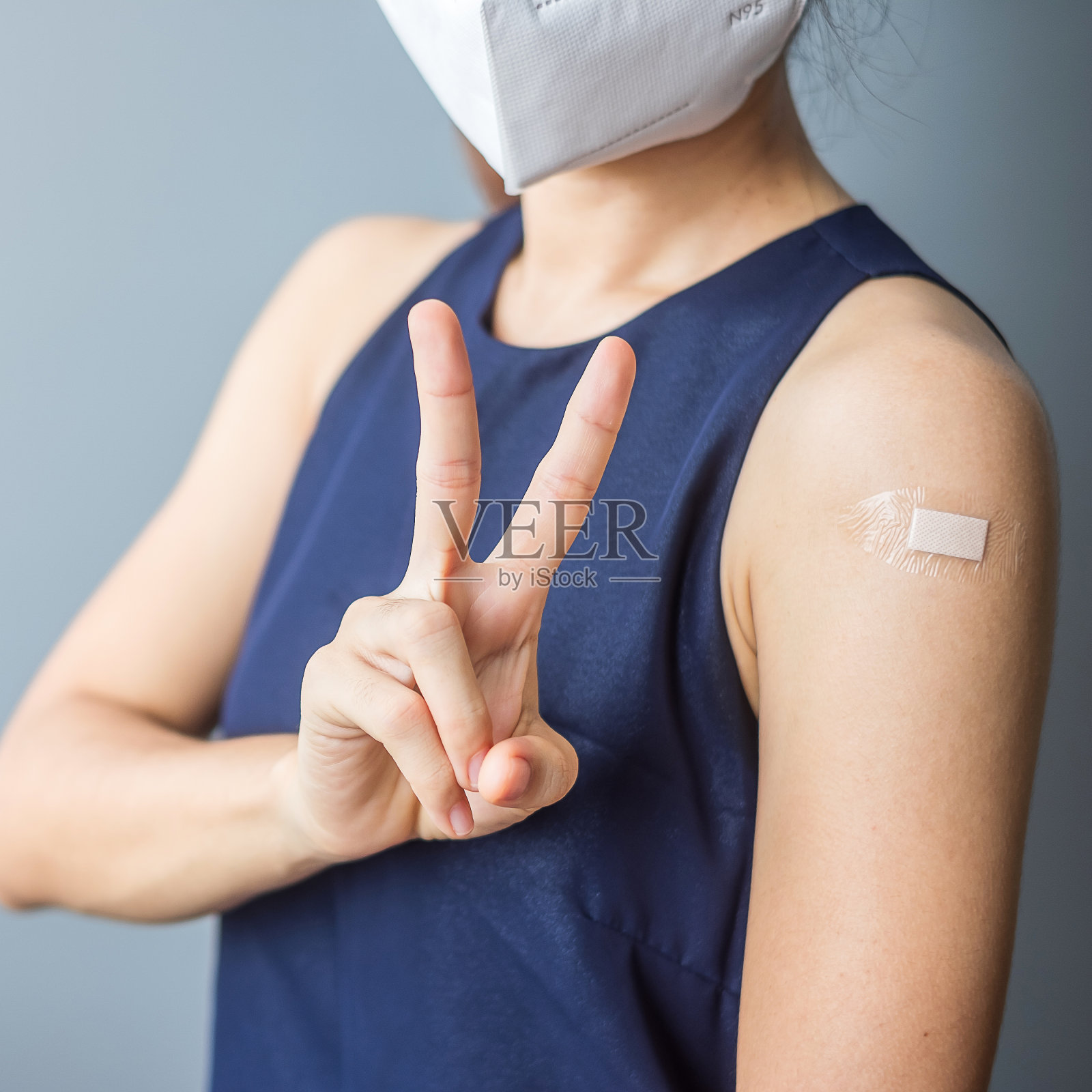 在接种新冠疫苗后，一名快乐的女性打着“胜利”的标志，脸上缠着绷带。疫苗接种、群体免疫、副作用、效率、疫苗护照和冠状病毒大流行照片摄影图片