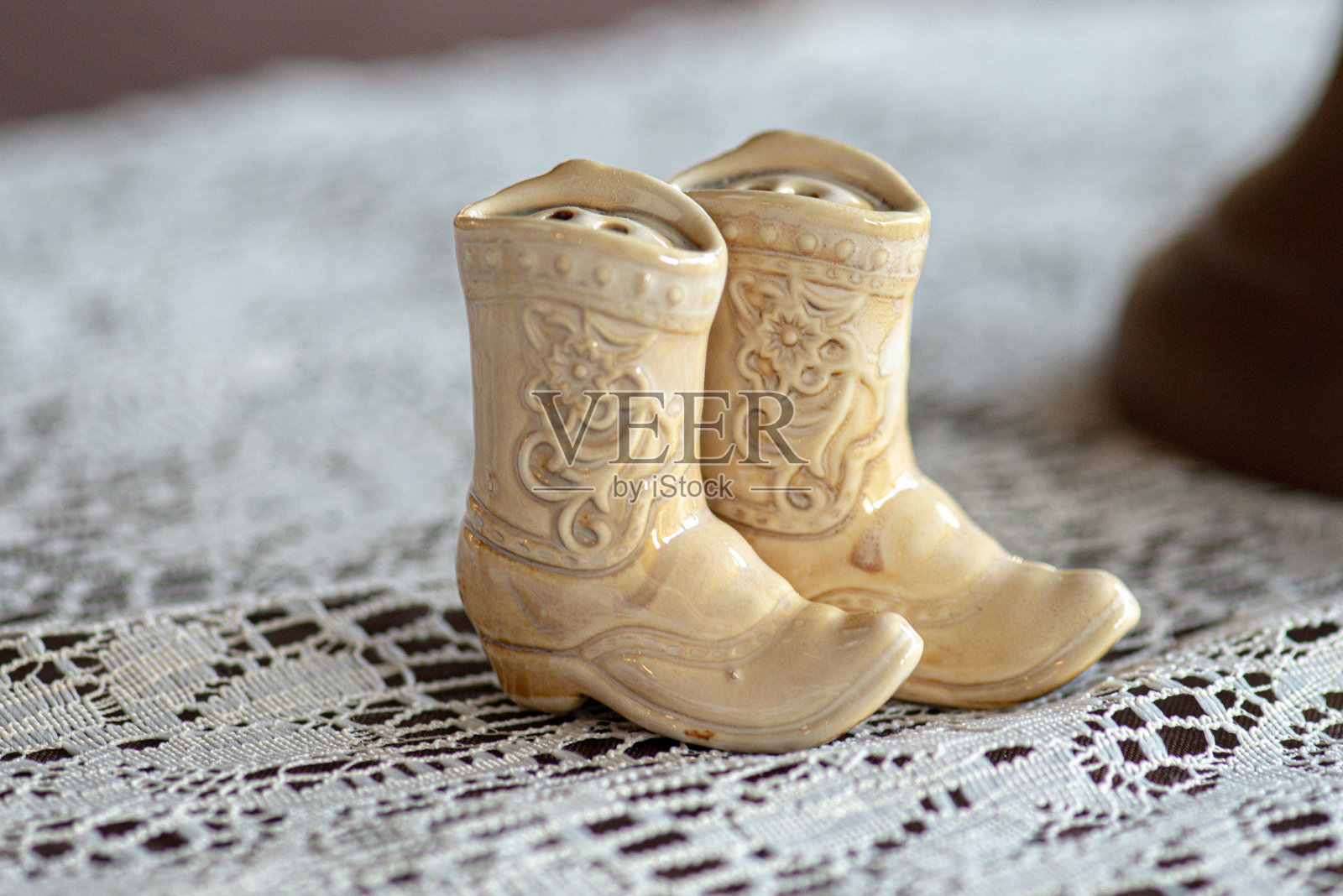 微型玻璃白色牛仔靴雕像在白色蕾丝表面照片摄影图片