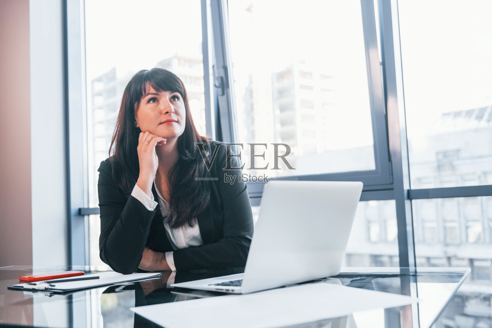 桌上放着笔记本电脑。穿着黑色正装的女人在现代办公室的室内照片摄影图片