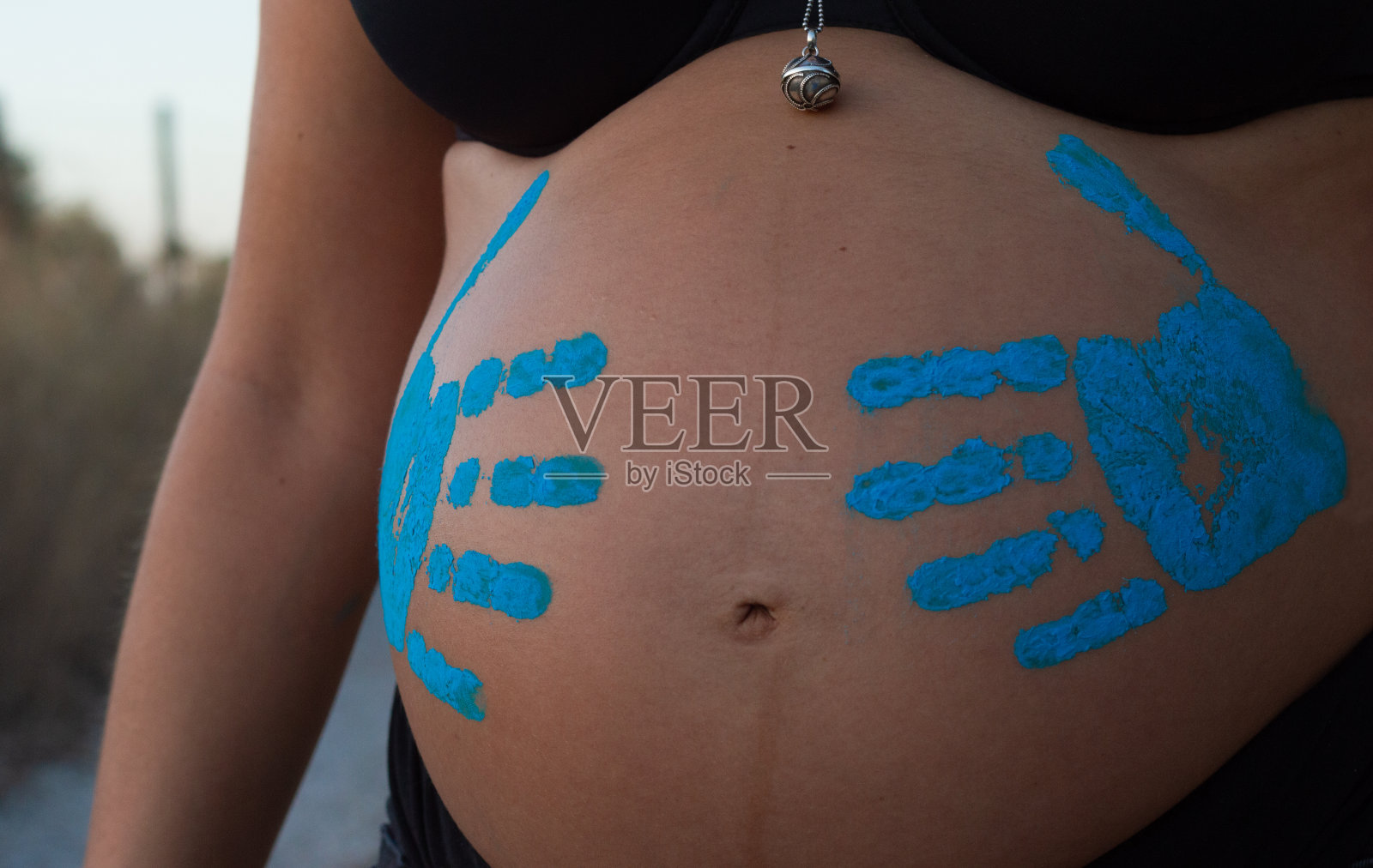 近距离拍摄了一个无法辨认的孕妇，她的肚子上画着蓝色的手。照片摄影图片