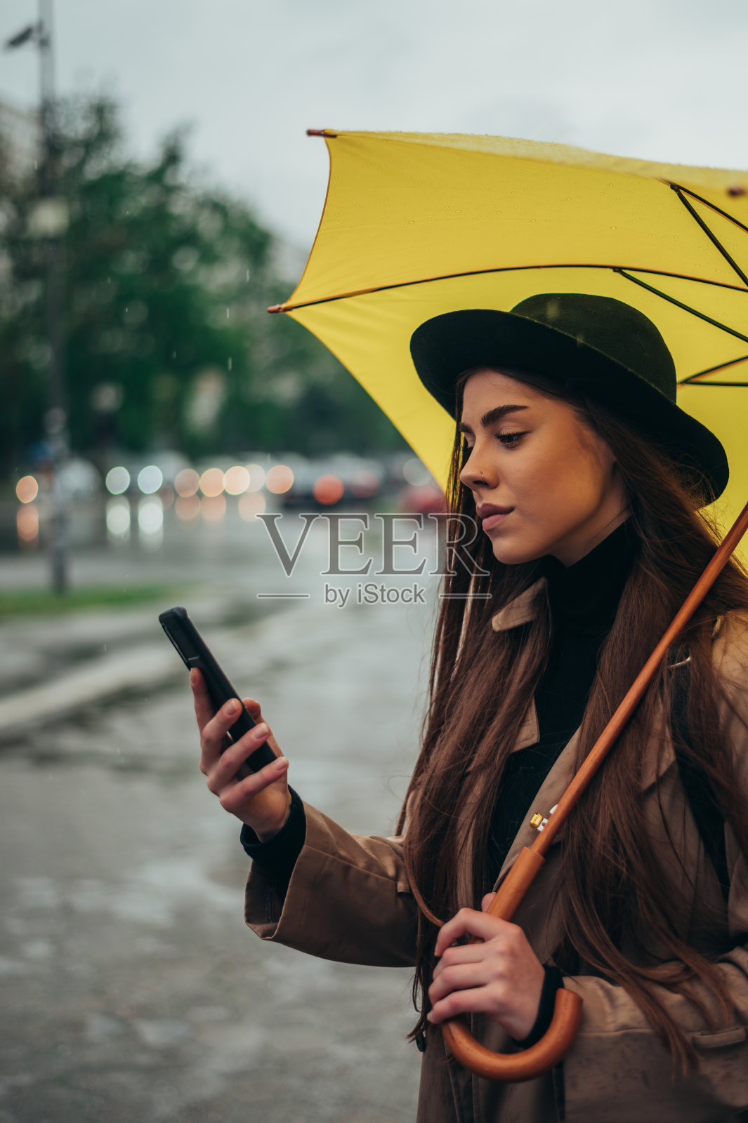年轻漂亮的女人拿着黄色雨伞，用着智能手机照片摄影图片
