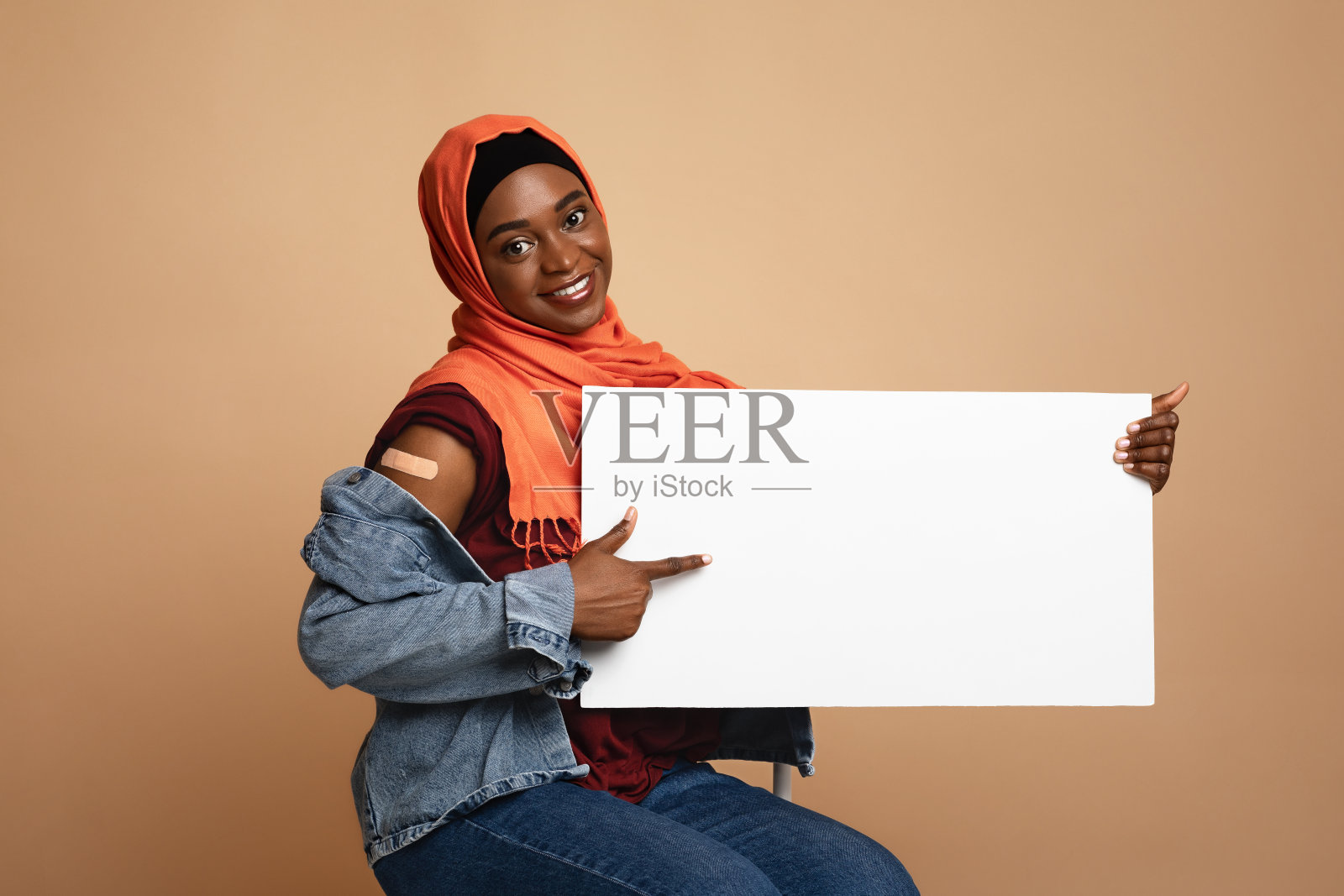 高兴的非洲裔美国穆斯林妇女接种疫苗，显示空的标语牌照片摄影图片