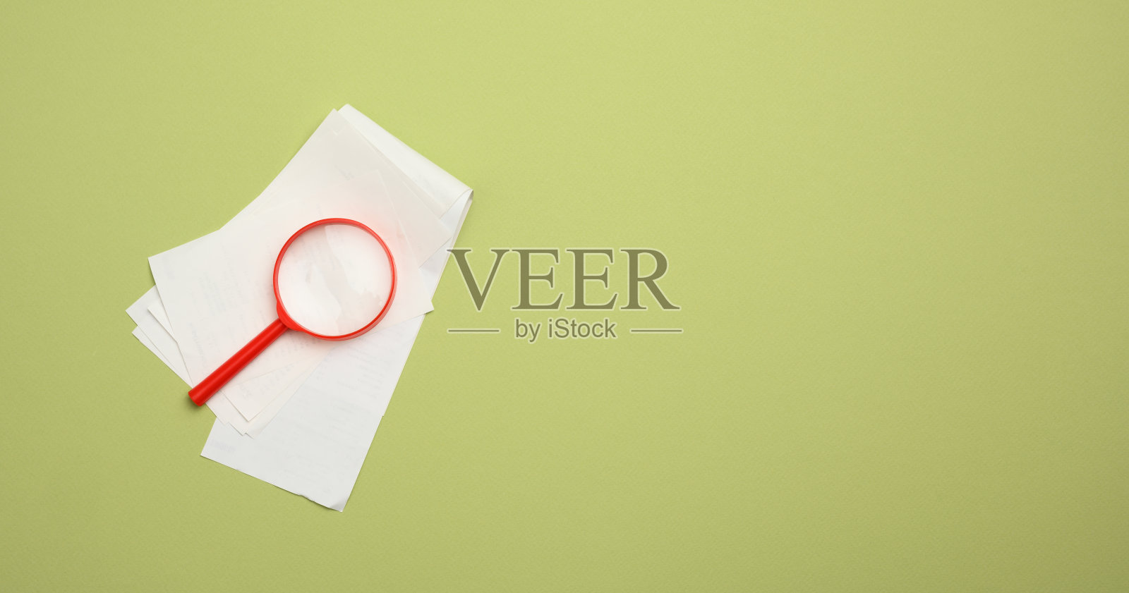 一叠纸质销售收据和绿色背景上的红色塑料放大镜。控制支出和收入的概念照片摄影图片