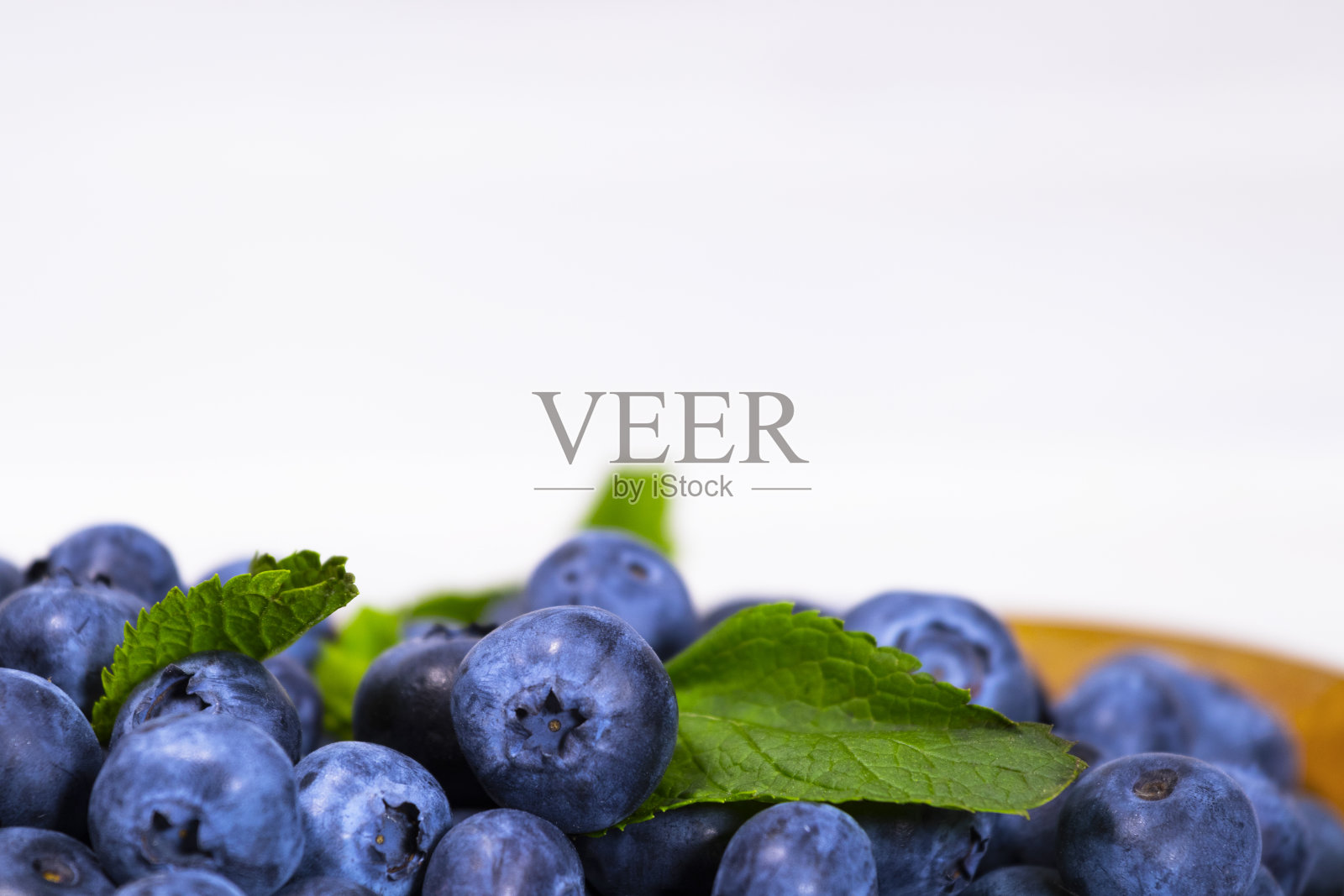 蓝莓与绿色薄荷叶在一个木制碗在一个白色的顶视图，夏天新鲜浆果，Copyspace照片摄影图片