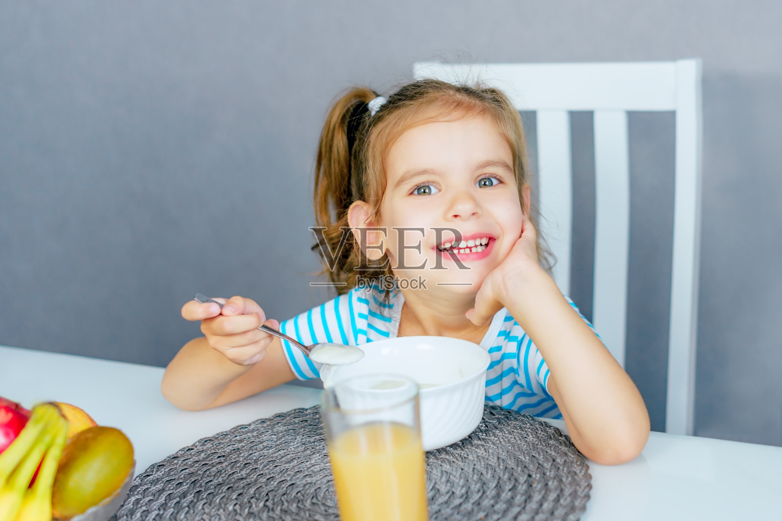 快乐的小女孩早上在厨房里喝早餐粥。健康饮食的概念。照片摄影图片