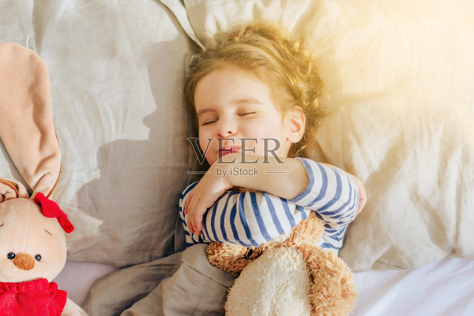 漂亮的小女孩和我最喜欢的玩具熊一起睡在我家的床上。照片摄影图片