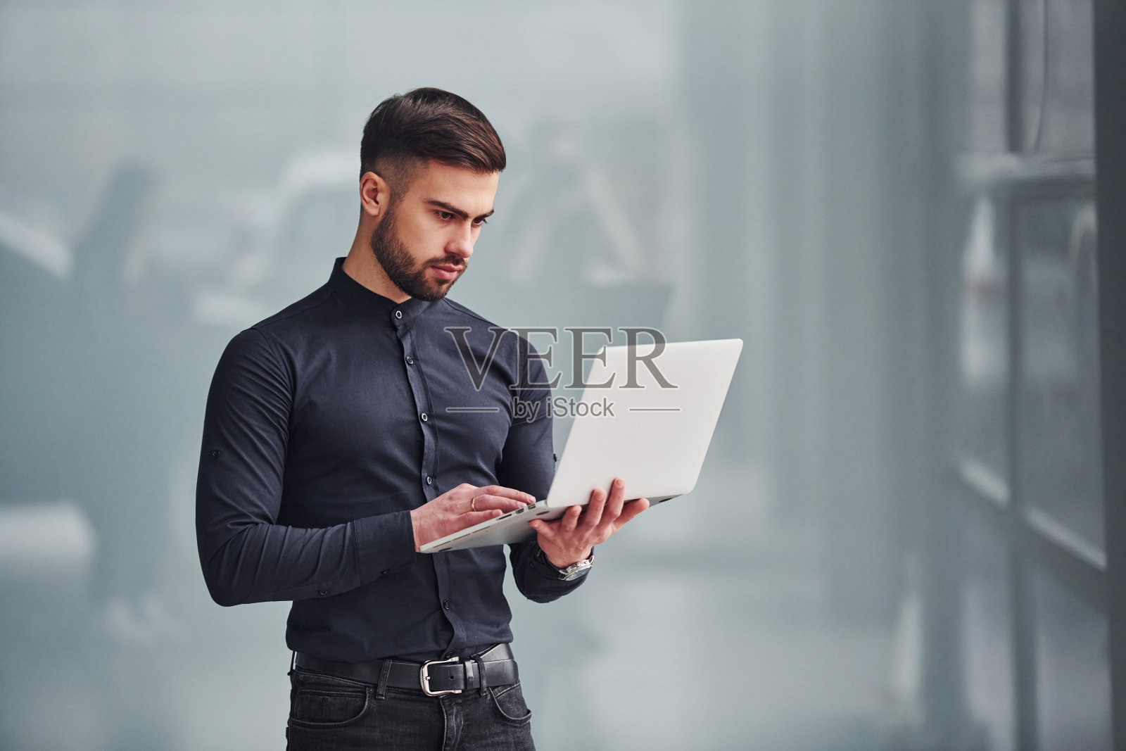 年轻的大胡子，穿着优雅的衣服，站在室内灰色的背景下照片摄影图片