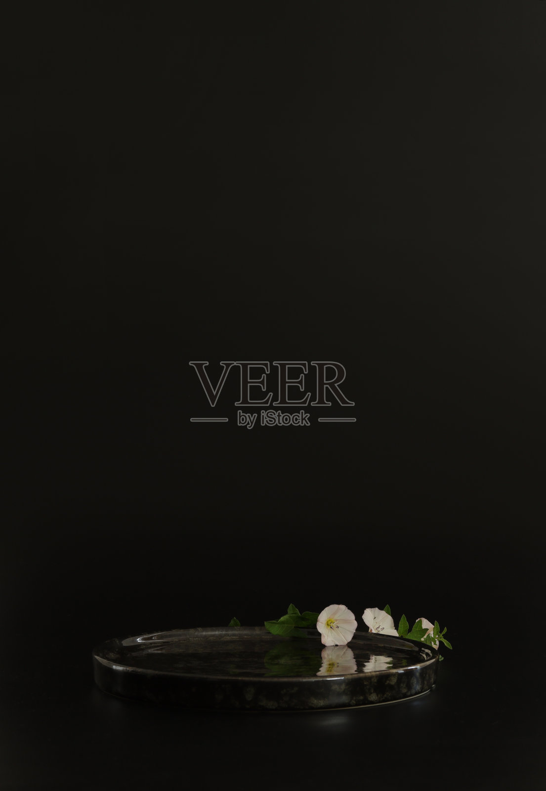 黑色的讲台上，黑色的背景上点缀着鲜花。讲台为产品，化妆品展示。创造性的模仿。放置美容产品的基座或平台。照片摄影图片