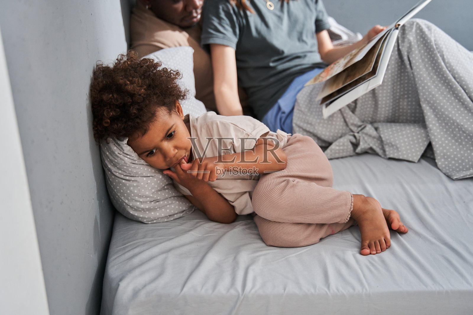 女孩躺在床上，靠近她的父母，听她的母亲如何读书照片摄影图片