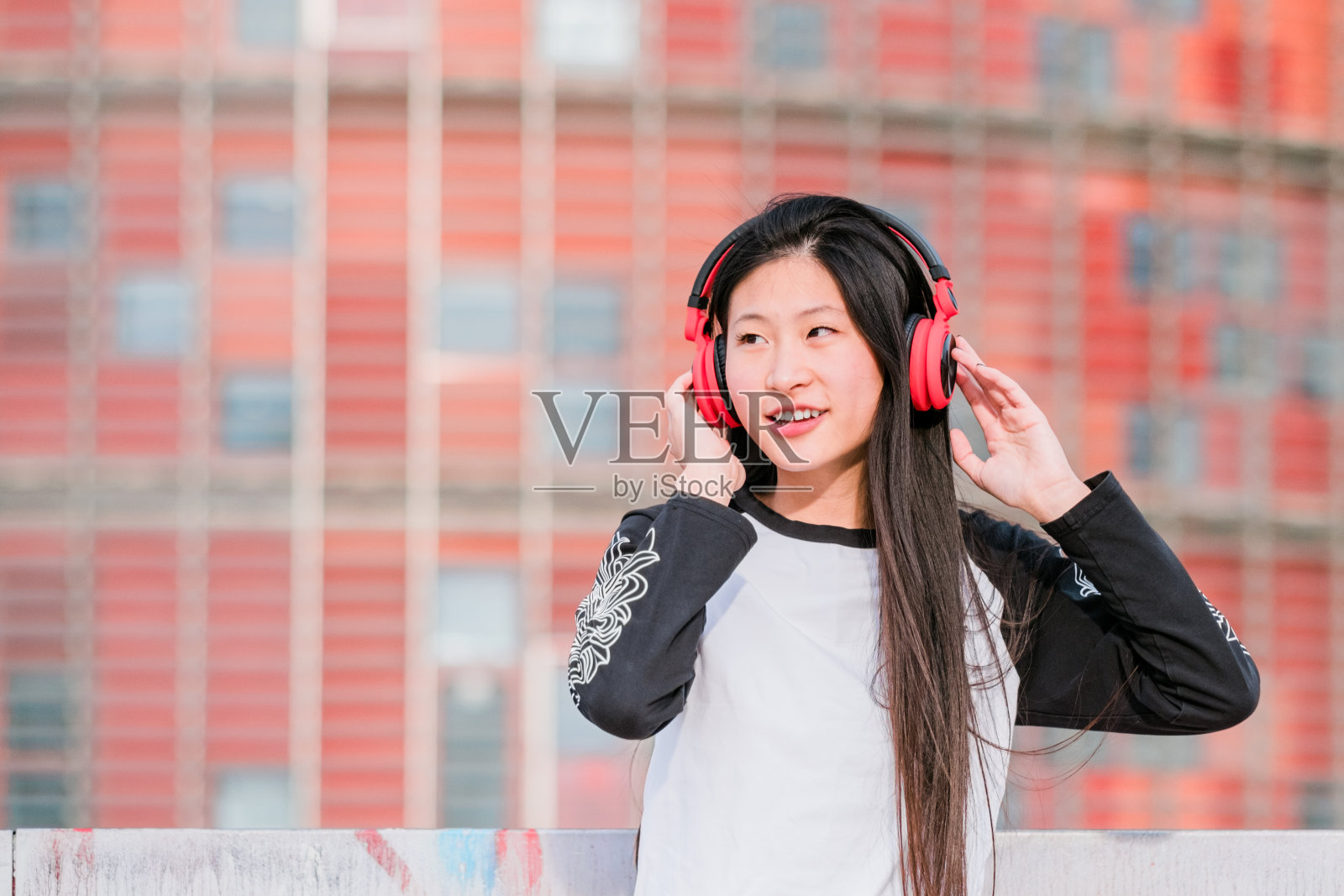 年轻快乐的亚洲女孩戴着耳机在城市街道上照片摄影图片