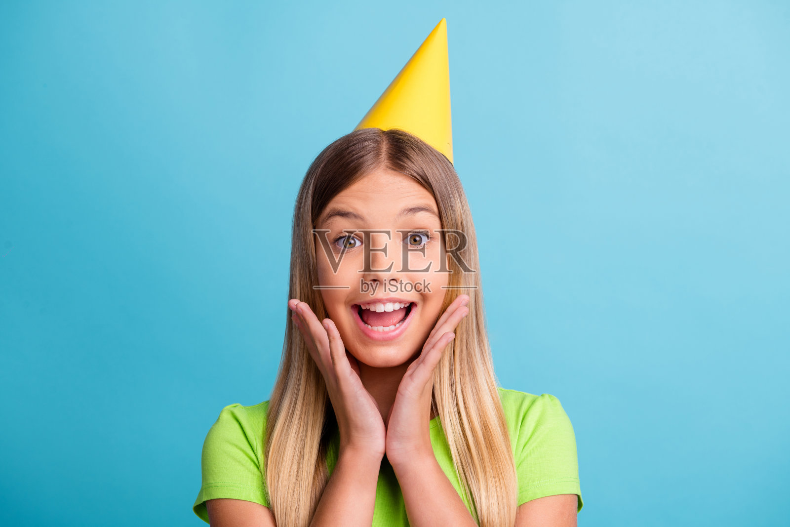 画像上年轻快乐兴奋震惊惊讶的女孩手牵脸颊戴锥形帽孤立在蓝色背景上照片摄影图片