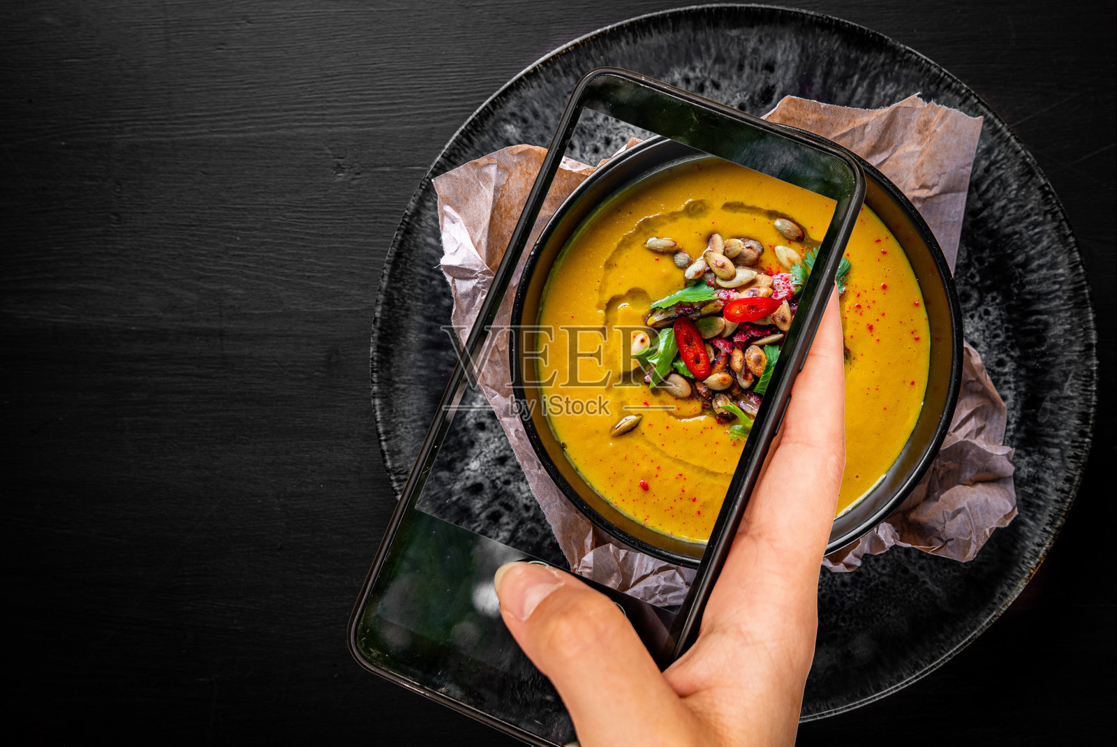 黑色木桌背景上黑色盘子里的南瓜汤。食物的照片照片摄影图片