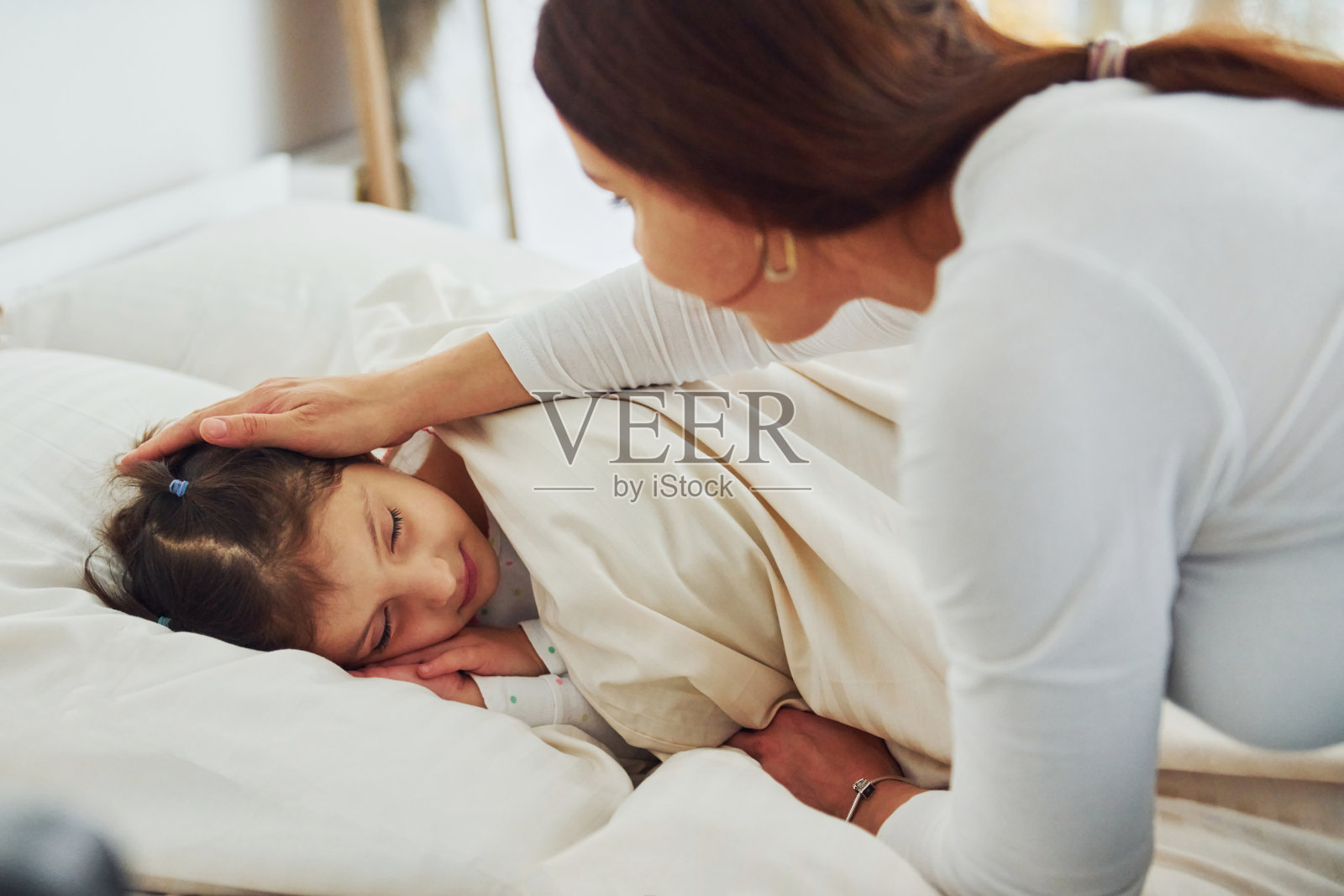 小女孩睡着了，妈妈看了看她。白天漂亮的现代卧室的室内和设计照片摄影图片