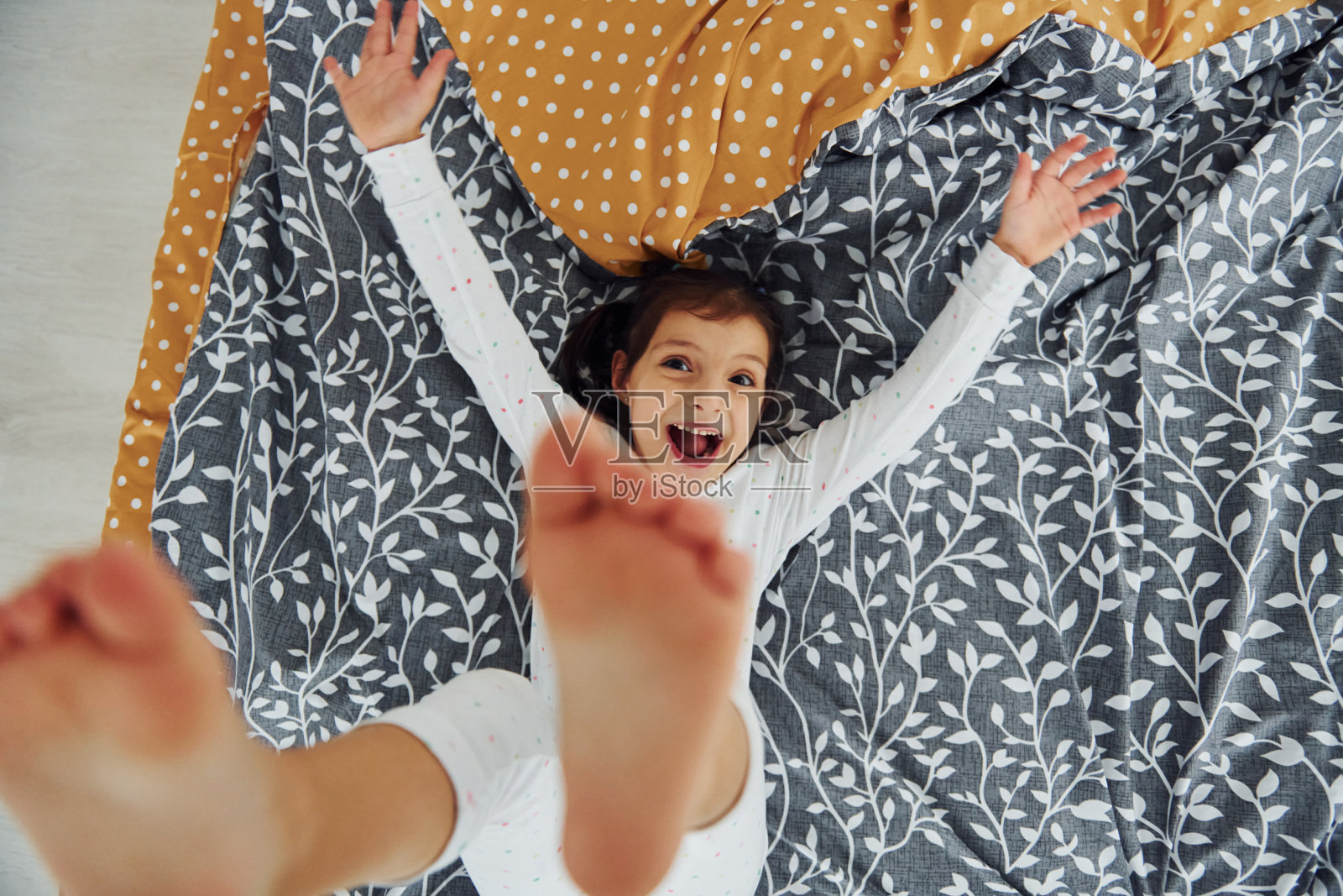 快乐的小女孩在床上玩的俯视图。白天漂亮的现代卧室的室内和设计照片摄影图片