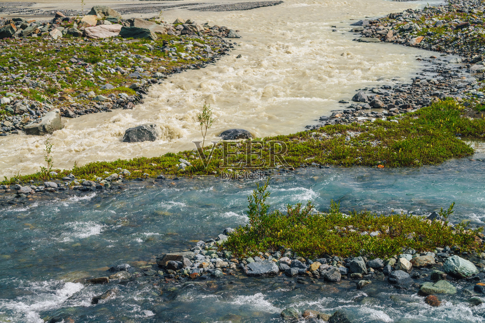 阳光明媚的高山景观与两种不同的山区河流汇合。美丽清澈的小溪流入肮脏的河流。两条不同的河流在丰富的植物群中交汇，形成了丰富多彩的山景。照片摄影图片