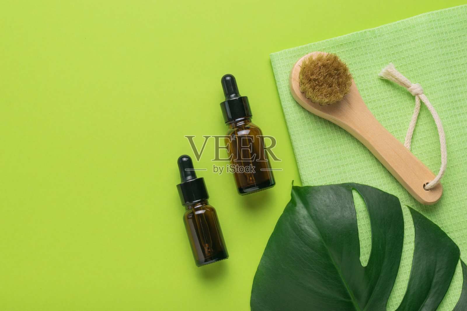 一张怪兽纸，两个带吸管的瓶子和一个绿色背景的手动面部按摩器。水疗中心。平的。照片摄影图片