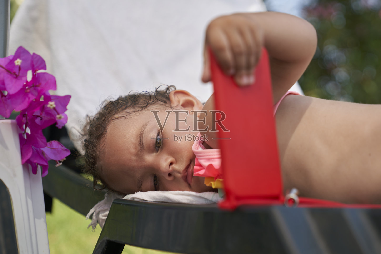 金发小女孩穿着粉红色的泳衣在海边玩手机照片摄影图片