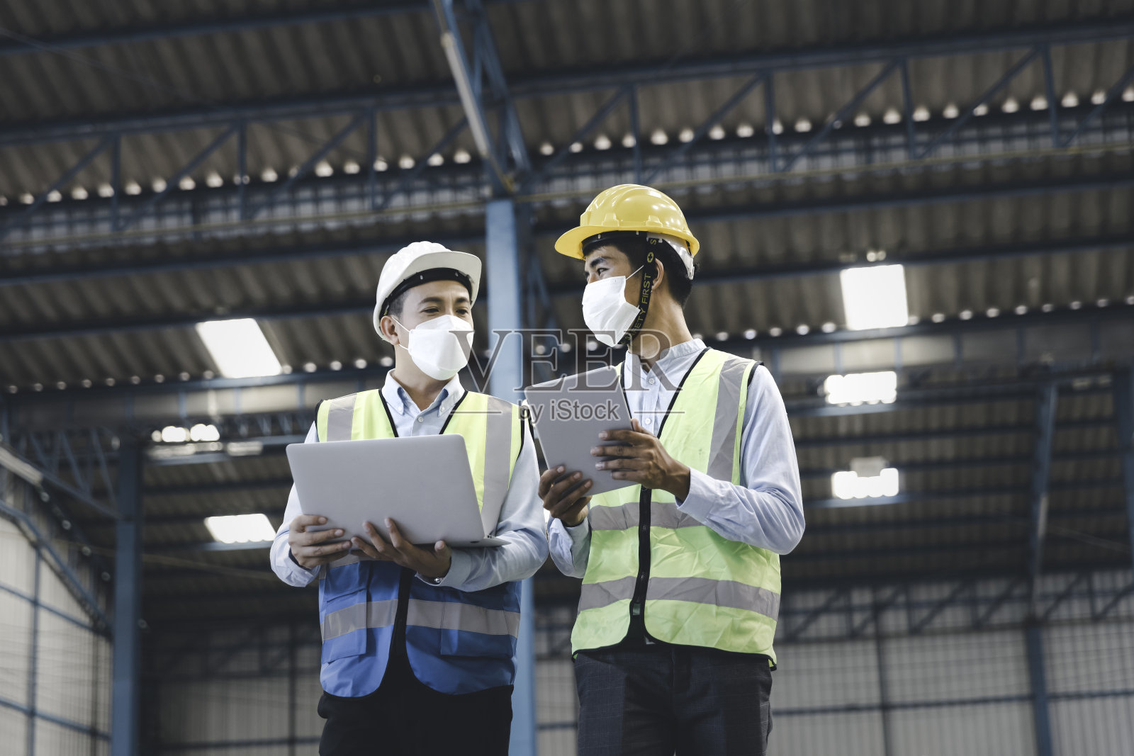 工厂经理和工程师戴着医用口罩和安全防护服，用笔记本电脑和数码平板电脑一起工作照片摄影图片