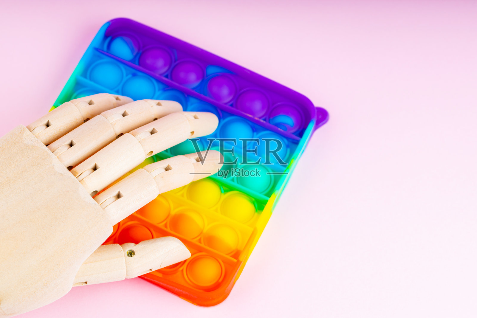 Pop it玩具和人工手在粉红色的背景。机器人点击弹出它。抗应激的概念。副本的空间。俯视图照片摄影图片