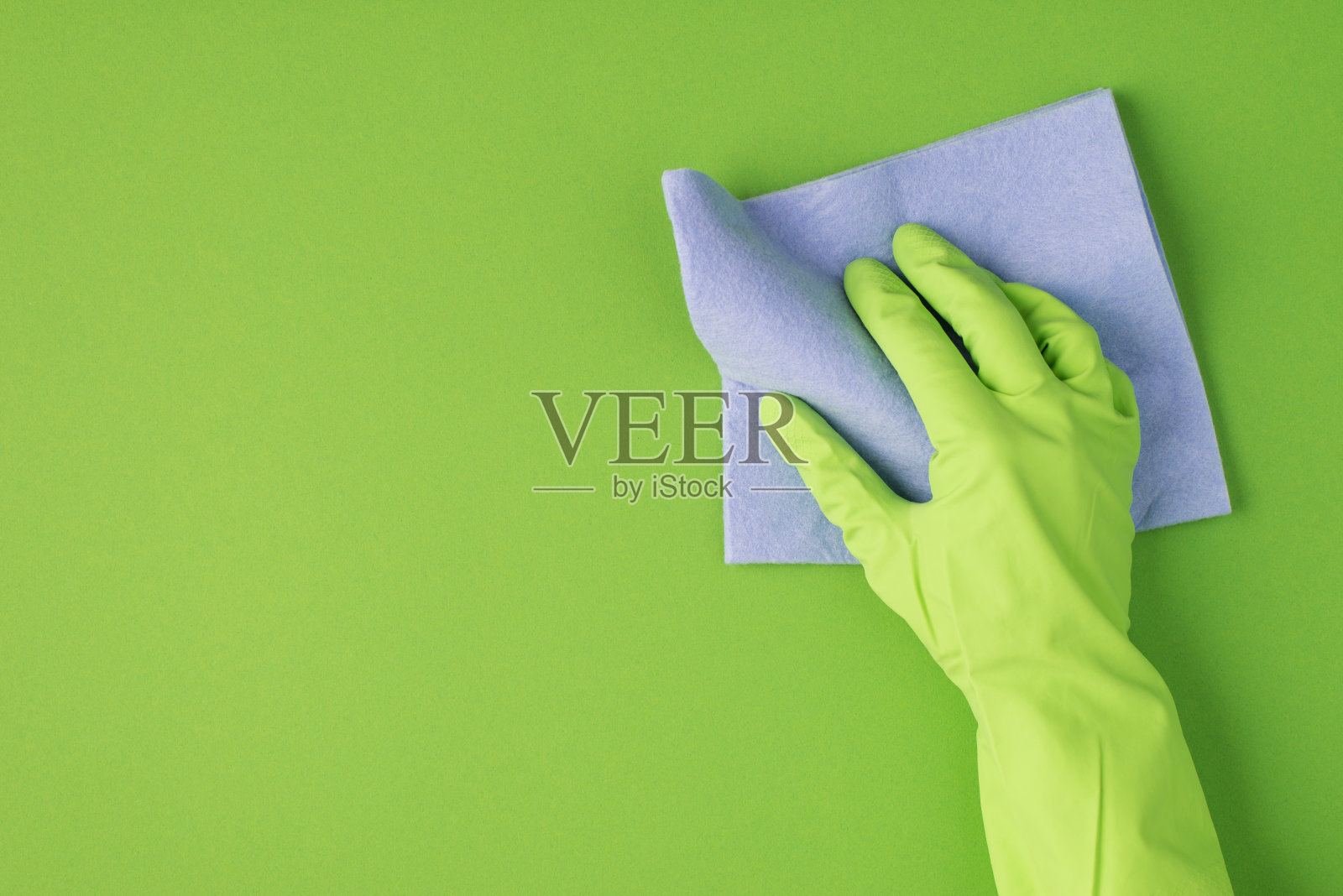 俯视图照片的手在绿色橡胶手套擦拭表面与紫丁香抹布孤立的绿色背景与copyspace在左边照片摄影图片