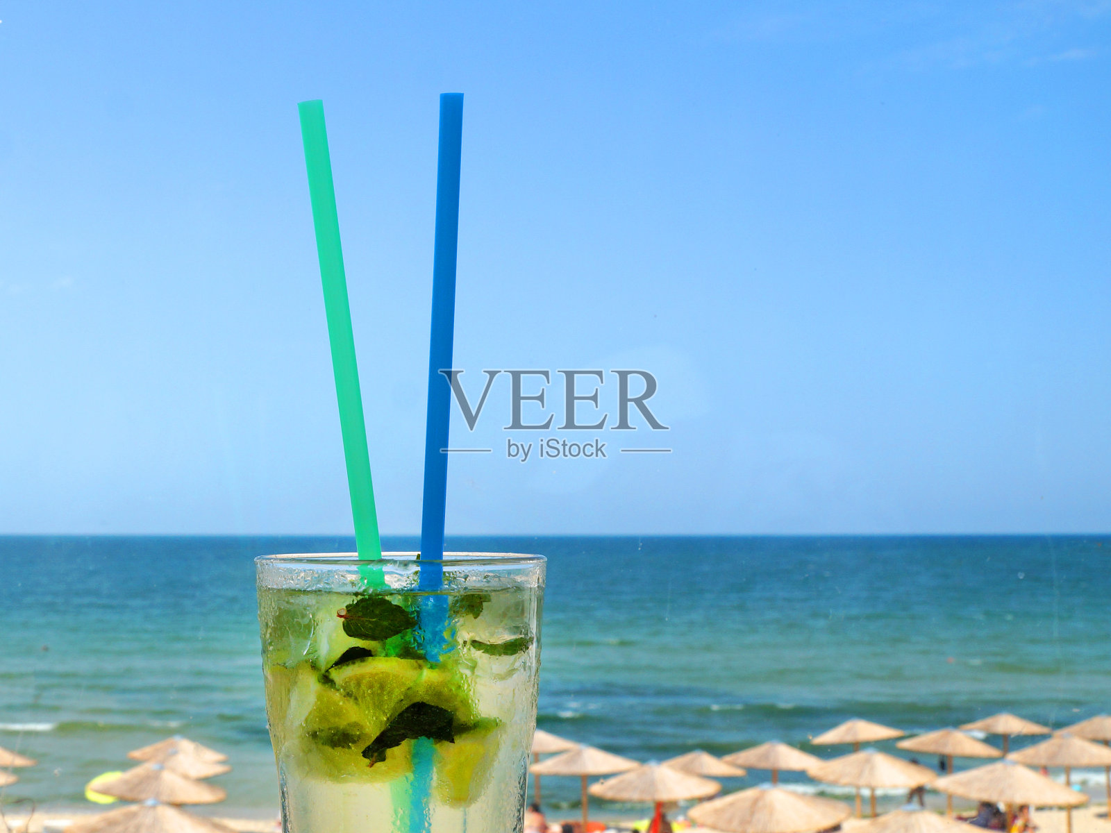 一杯莫吉托鸡尾酒，用吸管在地平线和海滩的背景下照片摄影图片