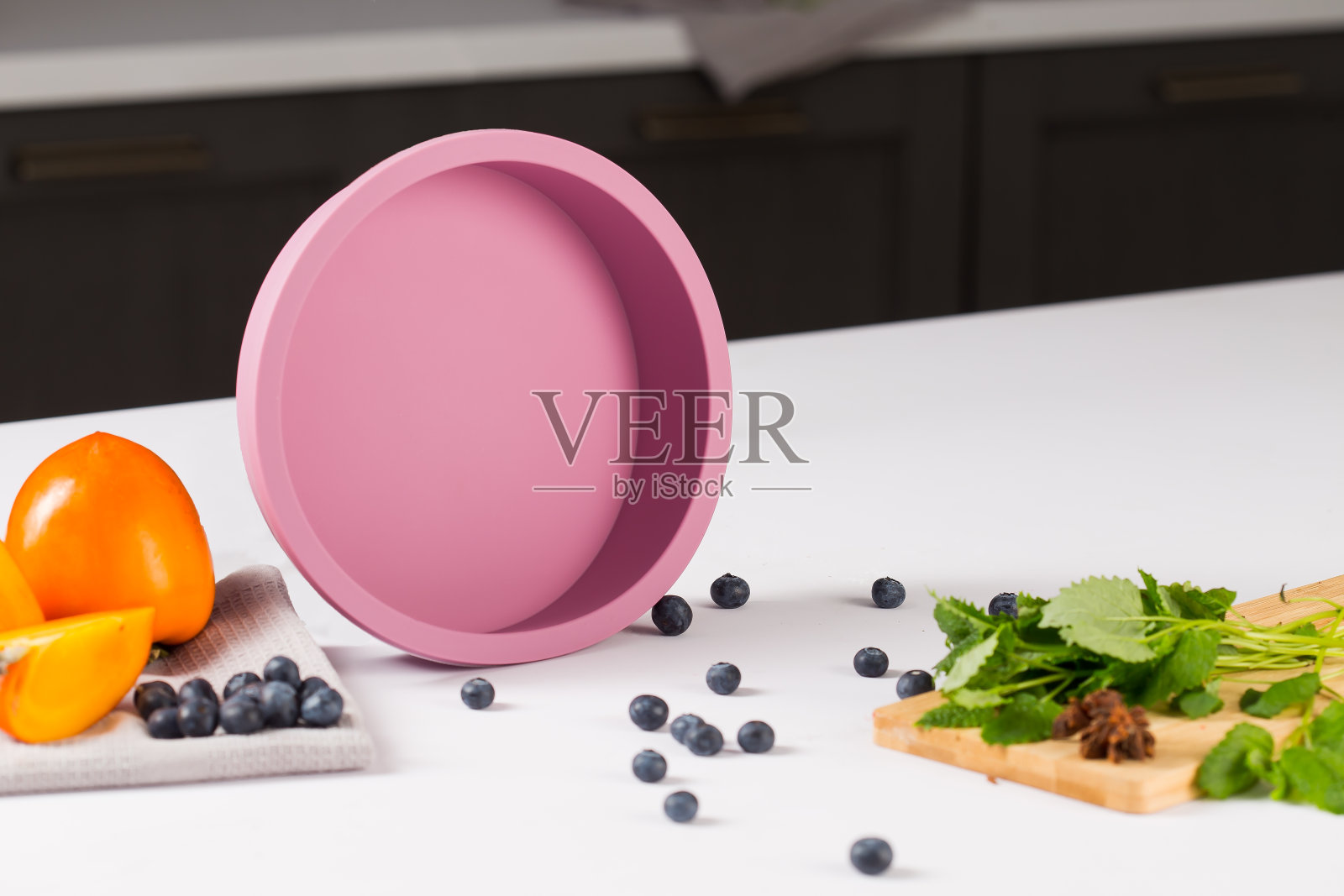 圆形紫色硅胶烤盘，蛋糕，附近的水果香蕉和橙子和绿色，在白色的桌子上，后面的厨房背景照片摄影图片