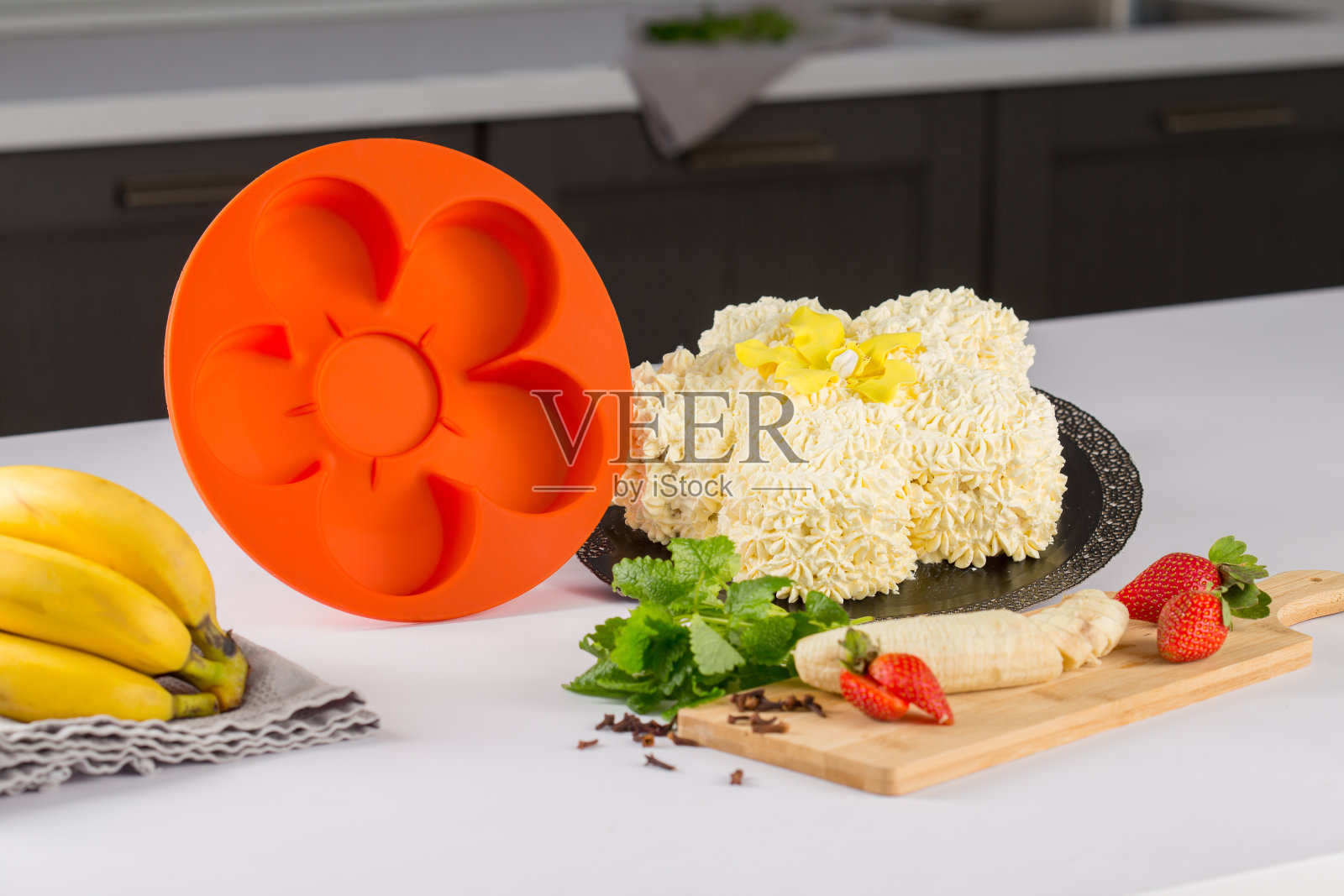 圆形紫色硅胶烤盘，蛋糕，附近的水果香蕉和橙子和绿色，在白色的桌子上，后面的厨房背景照片摄影图片