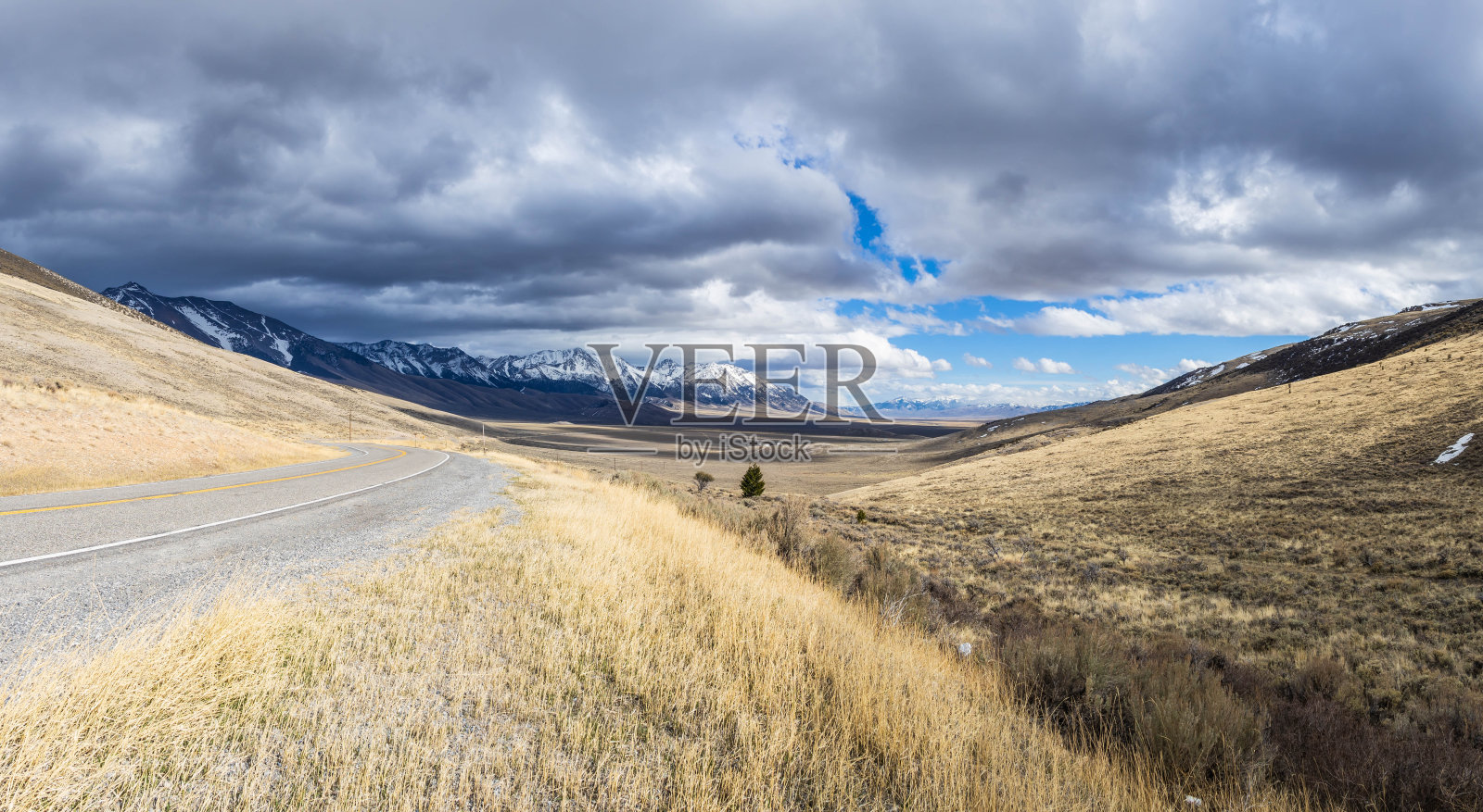 一条向左弯曲的道路展现出史诗般的山脉和草原景观，山顶被雪覆盖照片摄影图片