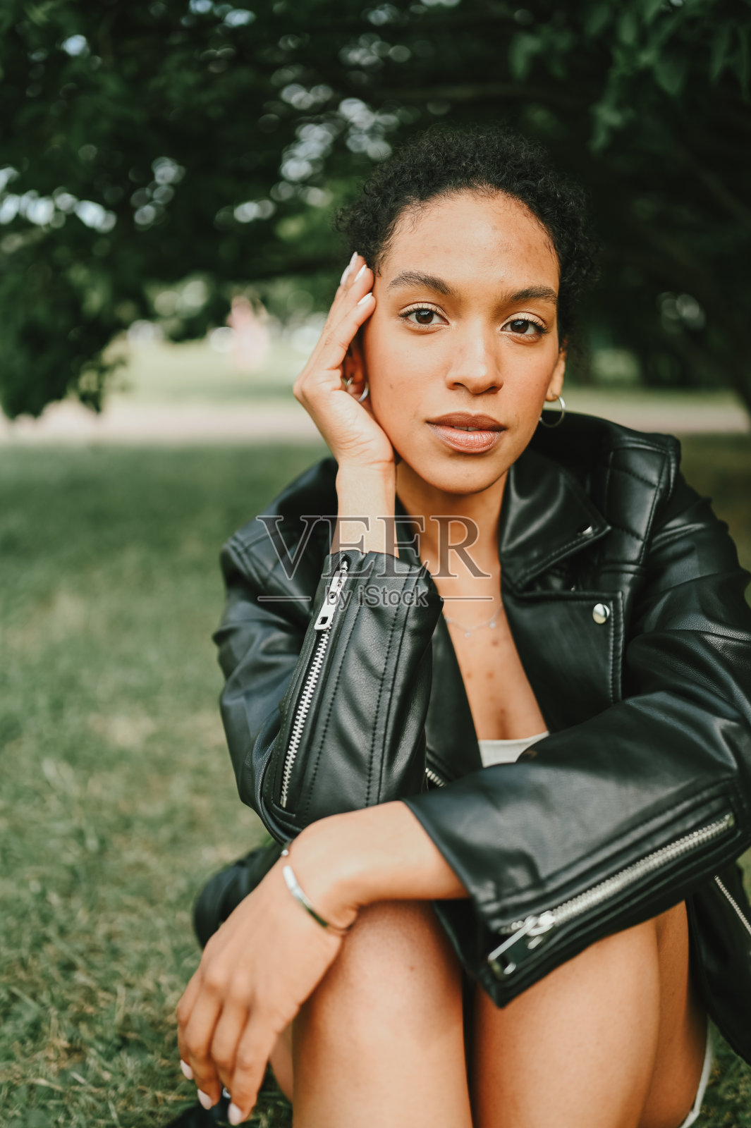 时尚肖像迷人的自信年轻的自然美非洲裔美国女人非洲式的头发在黑色皮夹克在自然公园在绿叶照片摄影图片