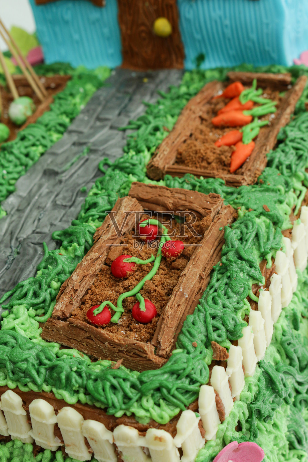 全帧图像的自制蛋糕设计为农舍和花园，黄油糖霜草和方糖糖霜通道，巧克力片种植的饼干屑土壤，方糖糖霜胡萝卜和番茄细节，聚焦前景照片摄影图片