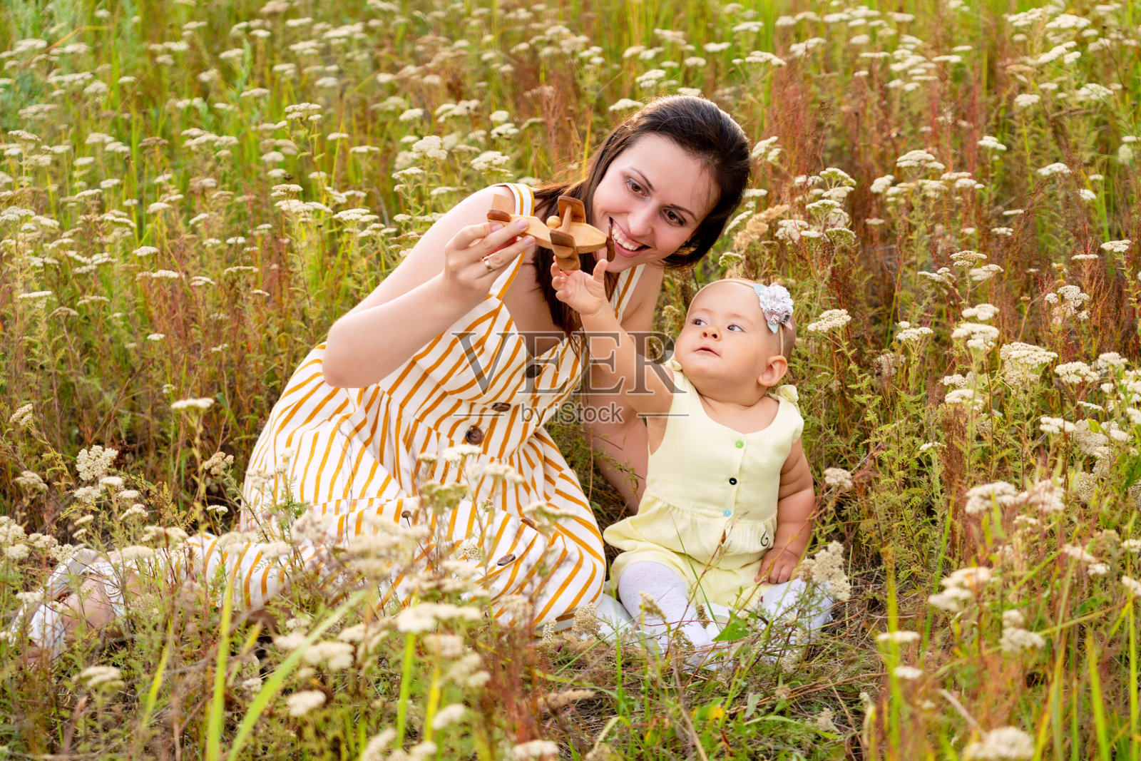 妈妈和新生婴儿在野花丛中玩木制双翼玩具飞机，乡村田野里快乐的母女照片摄影图片