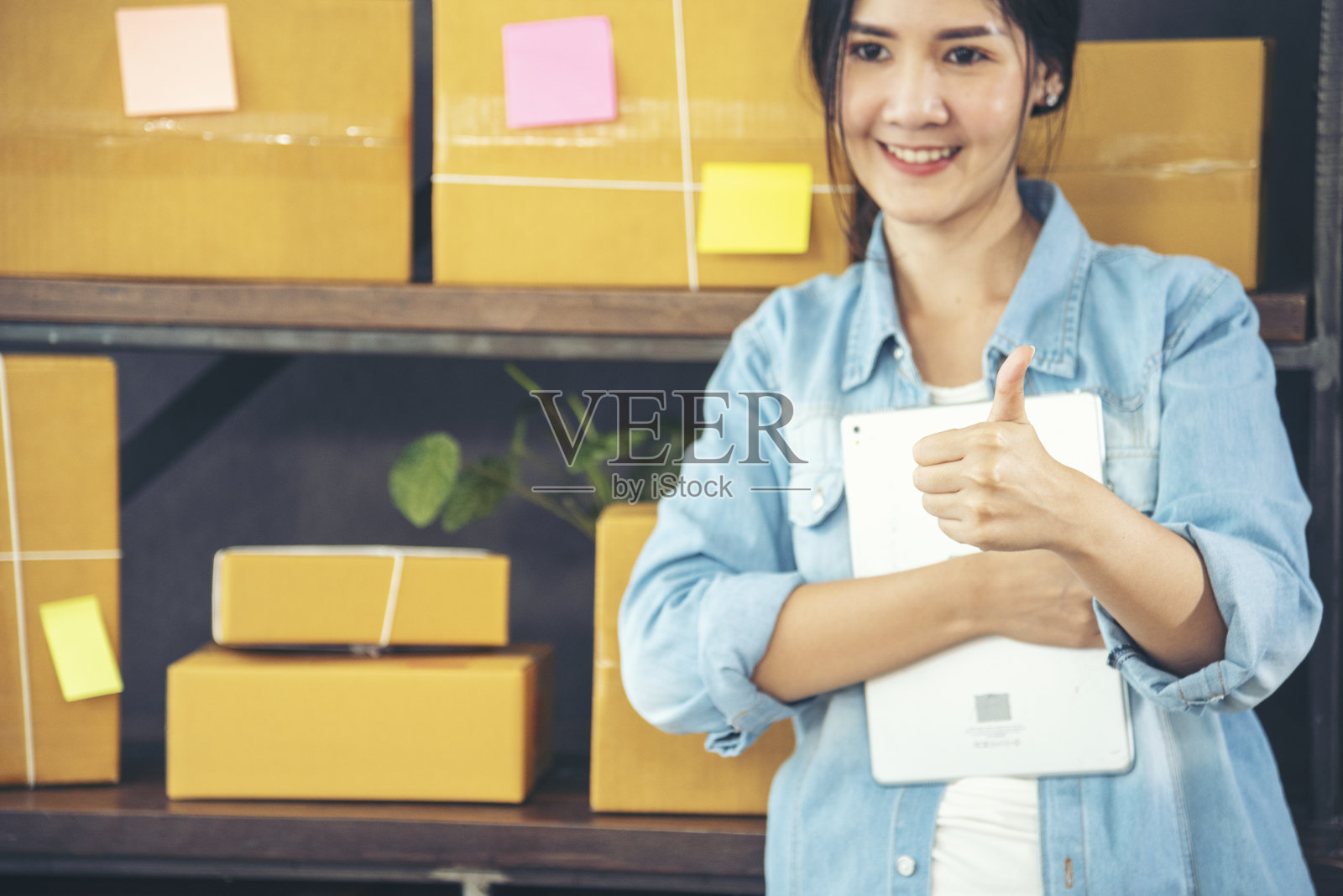 亚洲女性在家庭办公室创业。网上卖家企业家年轻的亚洲女性使用平板电脑查看网上订单。女人用药片检查库存货物供应快递包裹运输照片摄影图片