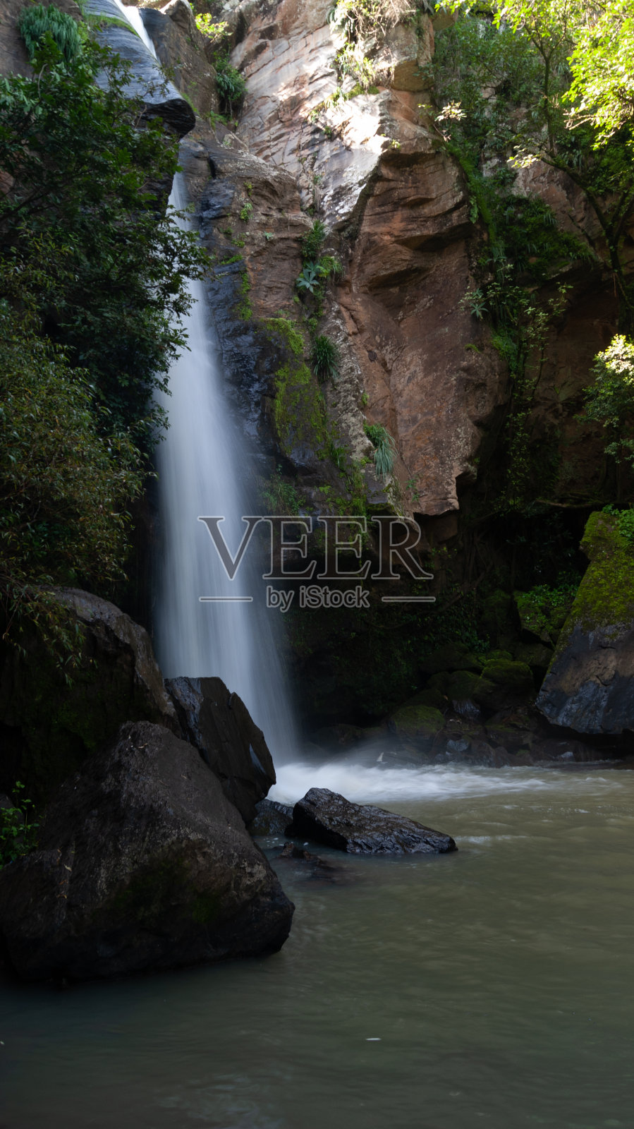 瀑布落入岩石和植被之间的泻湖照片摄影图片