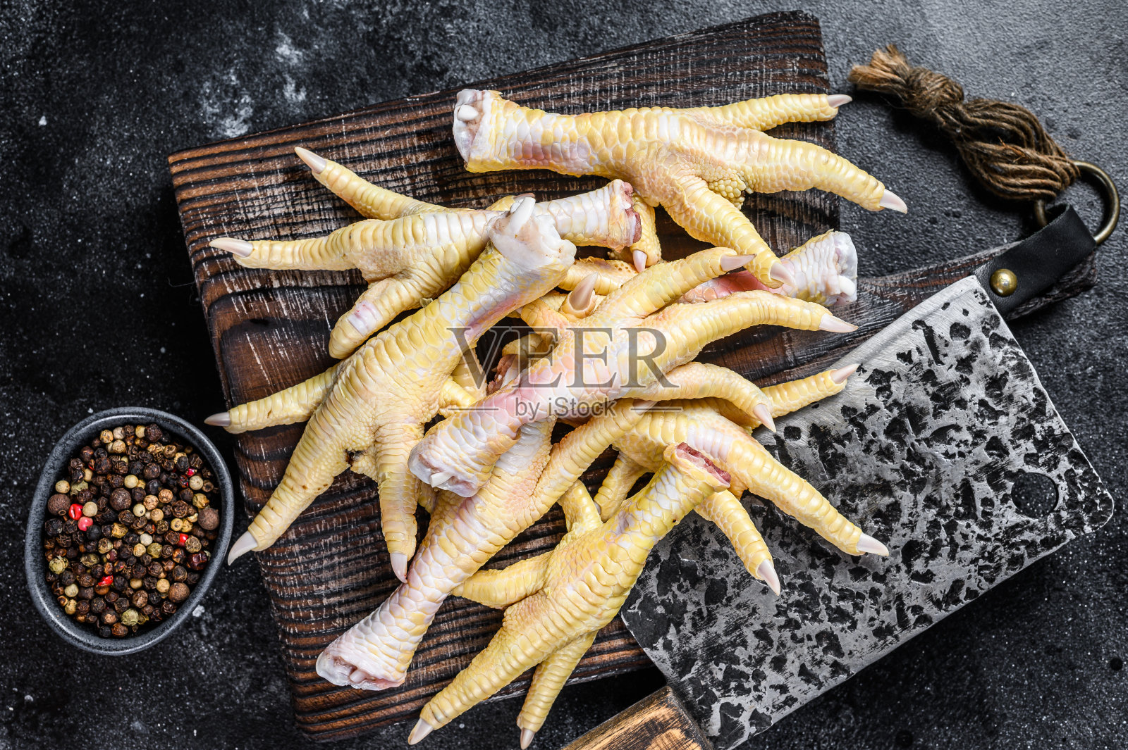 用切肉刀将生鸡爪放在砧板上。黑色背景。俯视图照片摄影图片