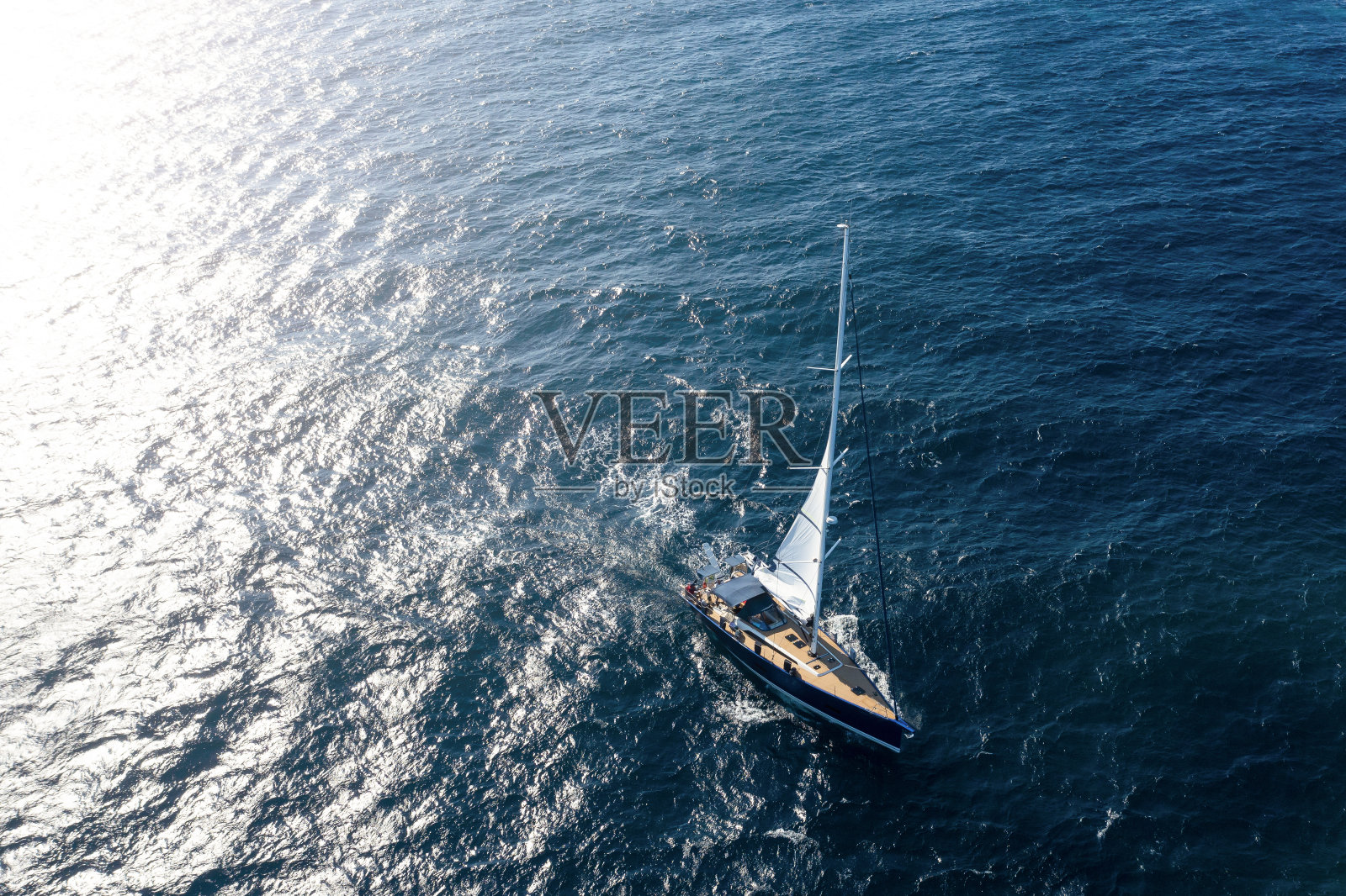 从上面看，令人惊叹的鸟瞰图的帆船航行在蓝色的水在日落。意大利撒丁岛的翡翠海岸。照片摄影图片