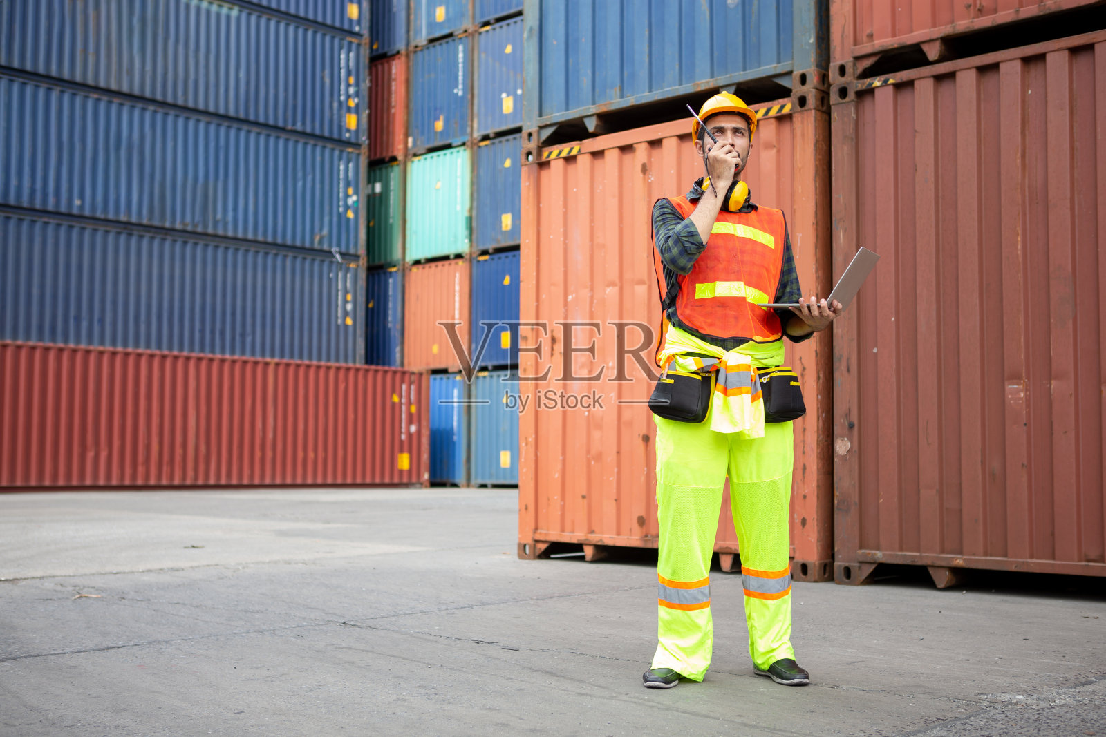 拉丁工头用手提电脑在对讲机上讲话，控制在仓库装卸集装箱，在货运船上装卸货物。拉美裔工程师照片摄影图片