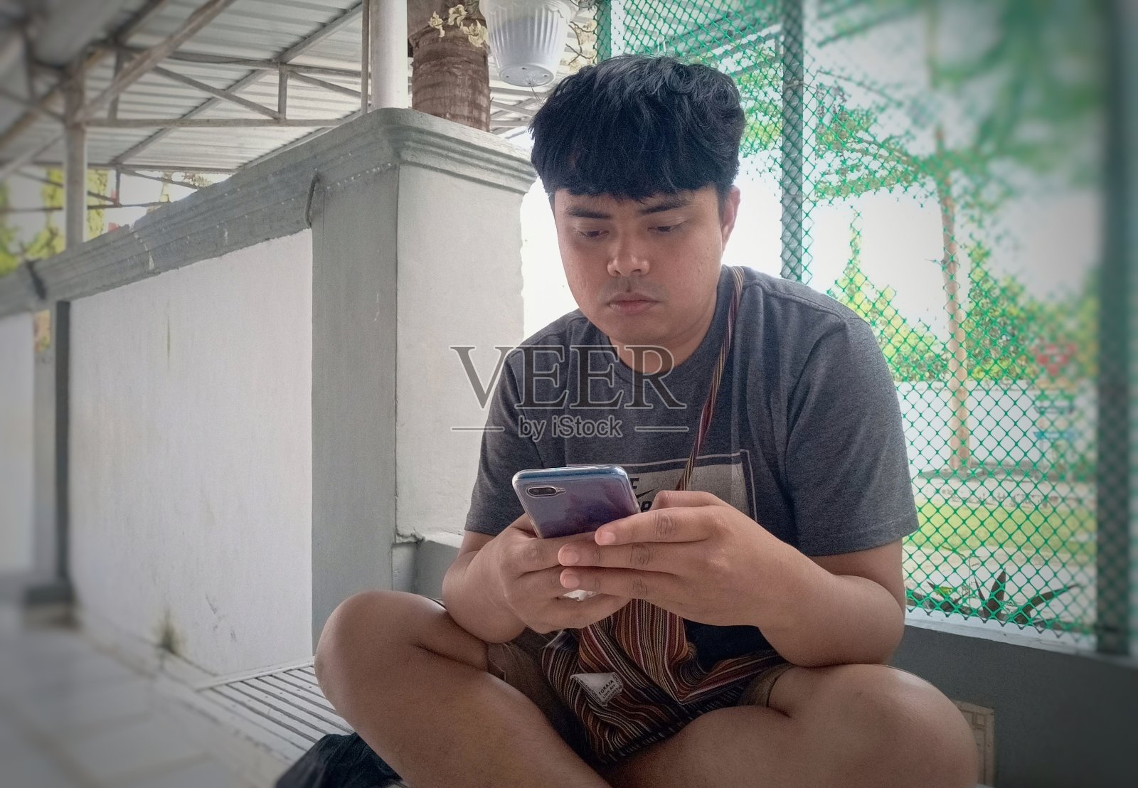 亚洲年轻人坐着玩智能手机照片摄影图片