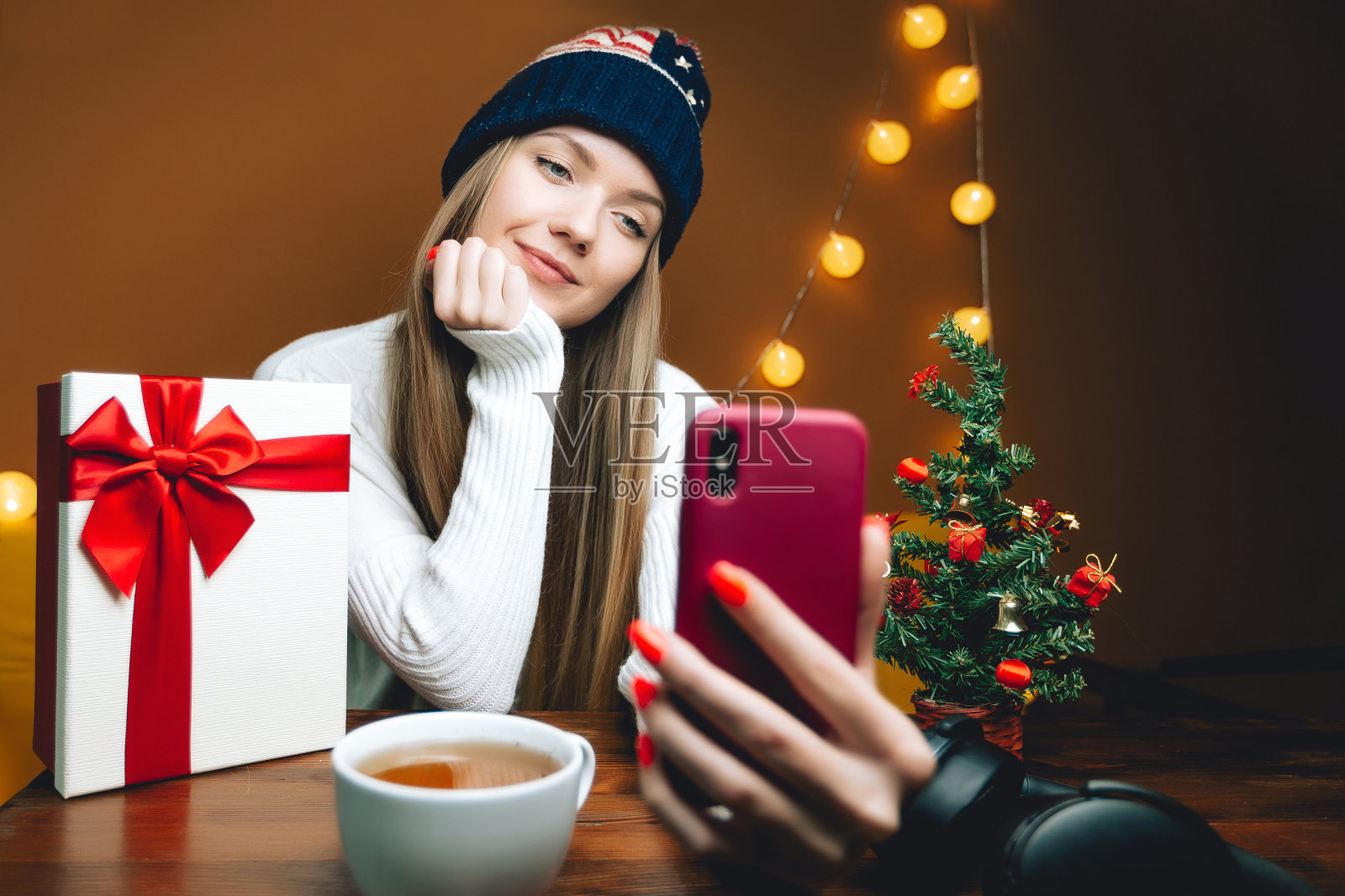 戴着美国帽子的好女人用智能手机自拍。木桌上的圣诞树照片摄影图片