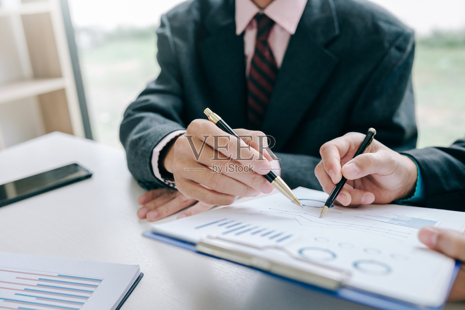 商人手持笔指着图表数据，显示投资者看到商业投资的增长。照片摄影图片