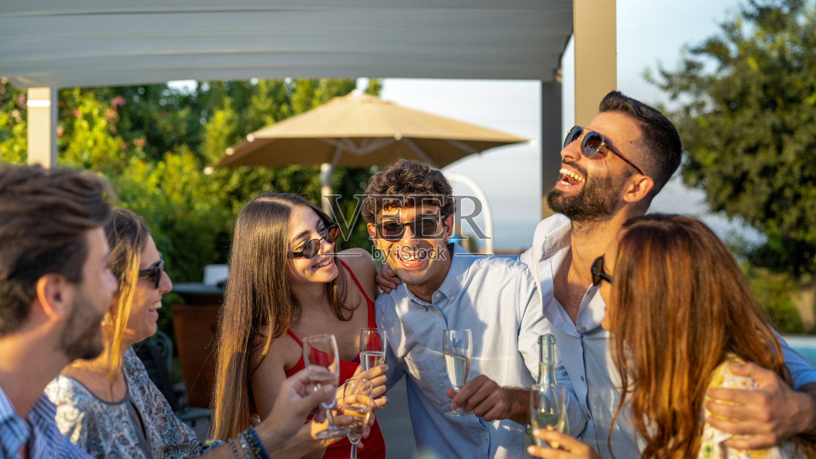 年轻人玩乐，日落户外聚会，一群朋友笑着，喝着白葡萄酒庆祝祝酒照片摄影图片