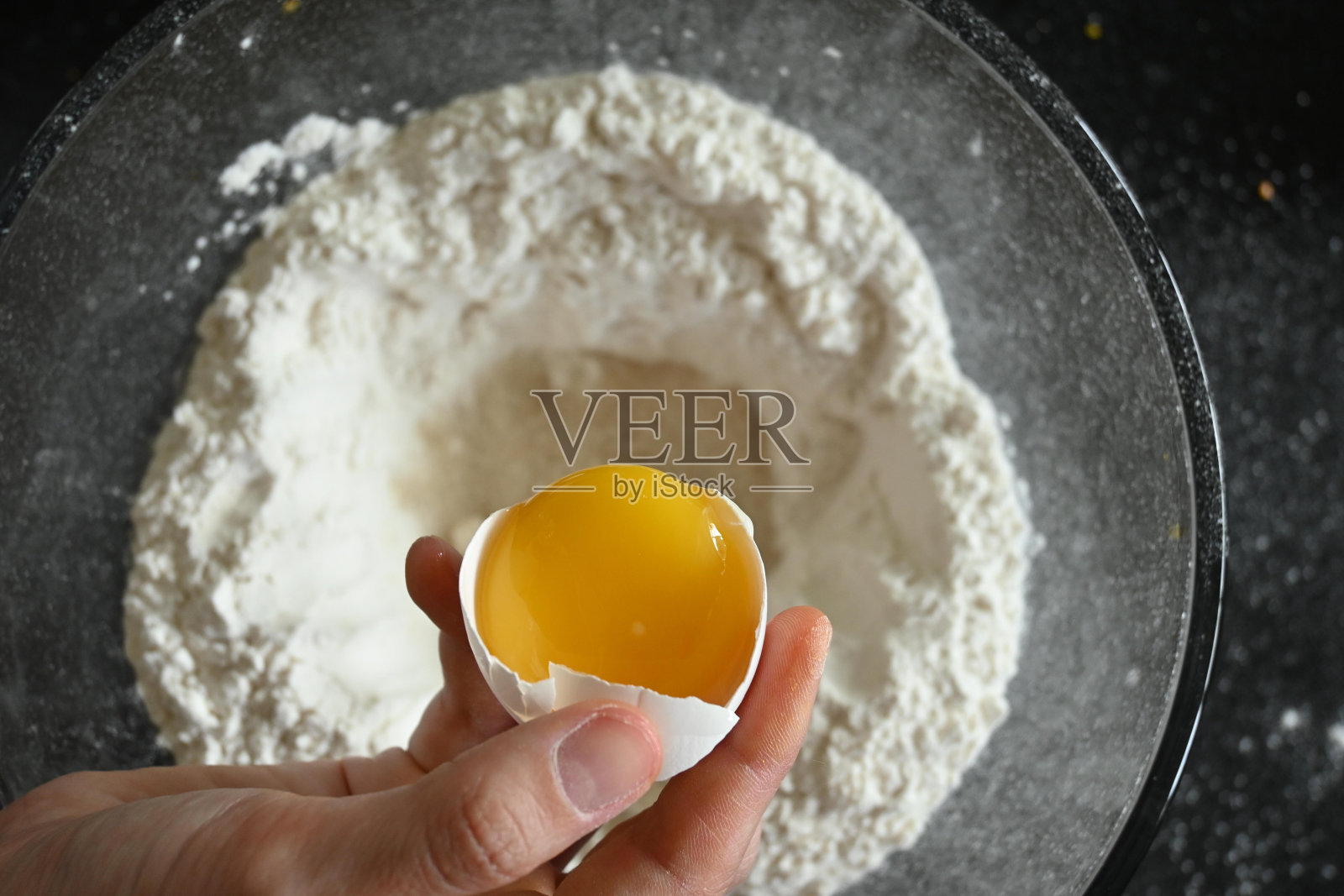 一个女人用手把鸡蛋倒在面粉上照片摄影图片