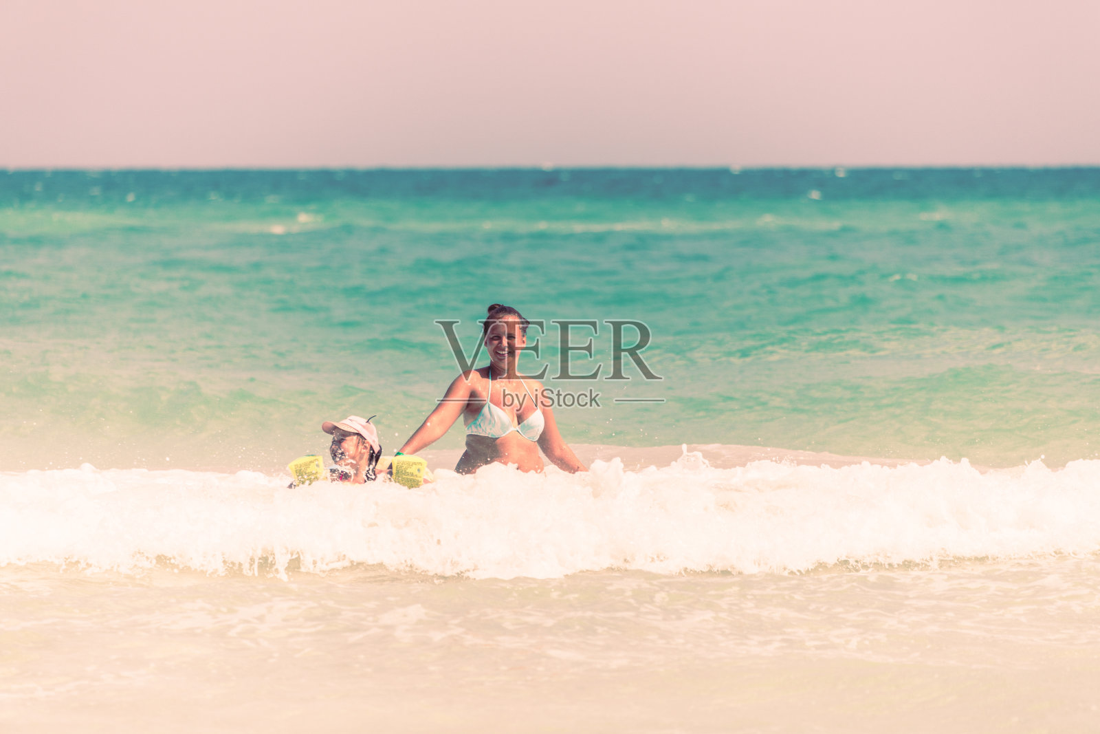 妈妈和女儿一起在海浪上游泳，妈妈教女儿游泳照片摄影图片