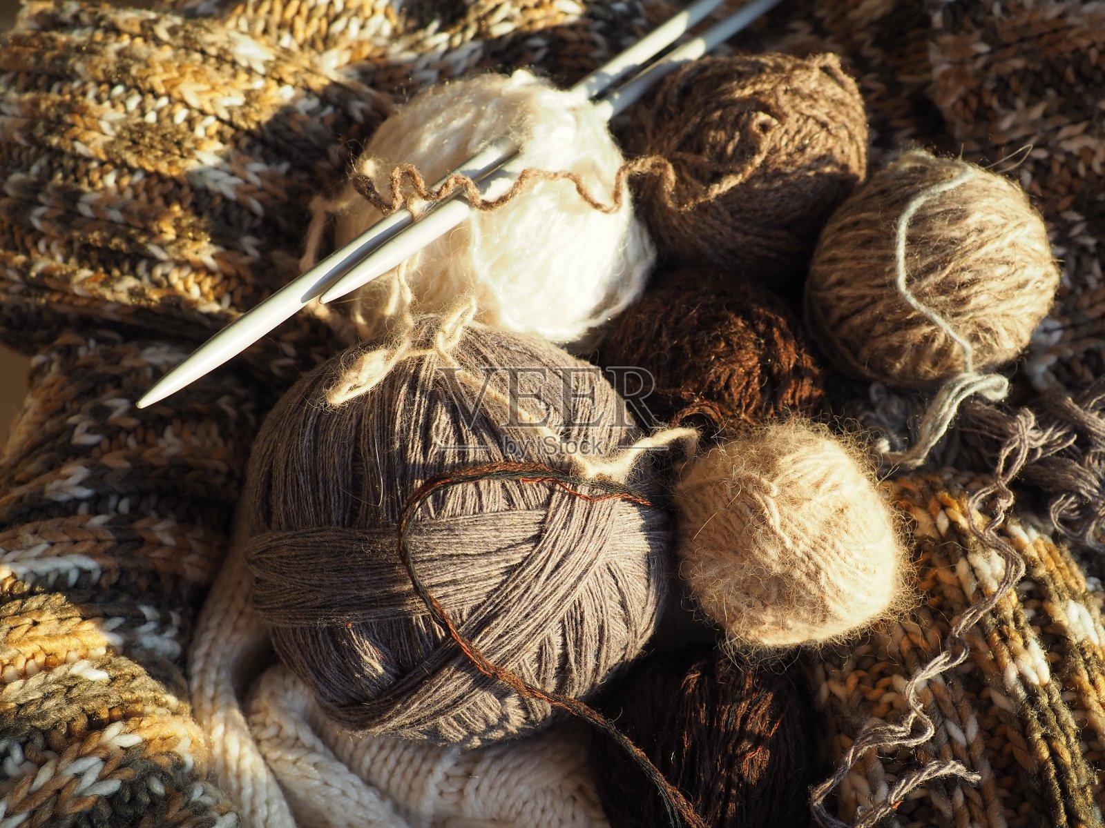 纱线球，针织衣服，针织针和钩针。把编织作为业余爱好。棕色，米色和白色丝线。散焦图像照片摄影图片