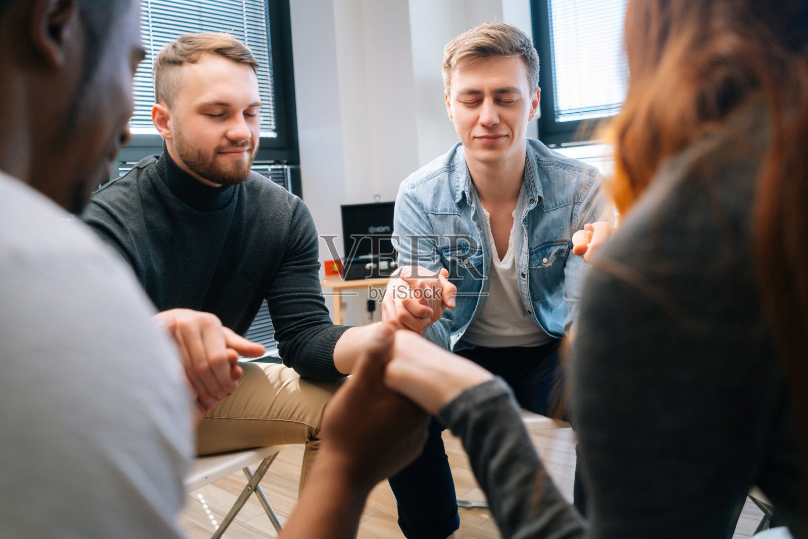 一群多元、多民族的年轻人在心理治疗过程中手牵着手，一起冥想和解决心理问题。照片摄影图片