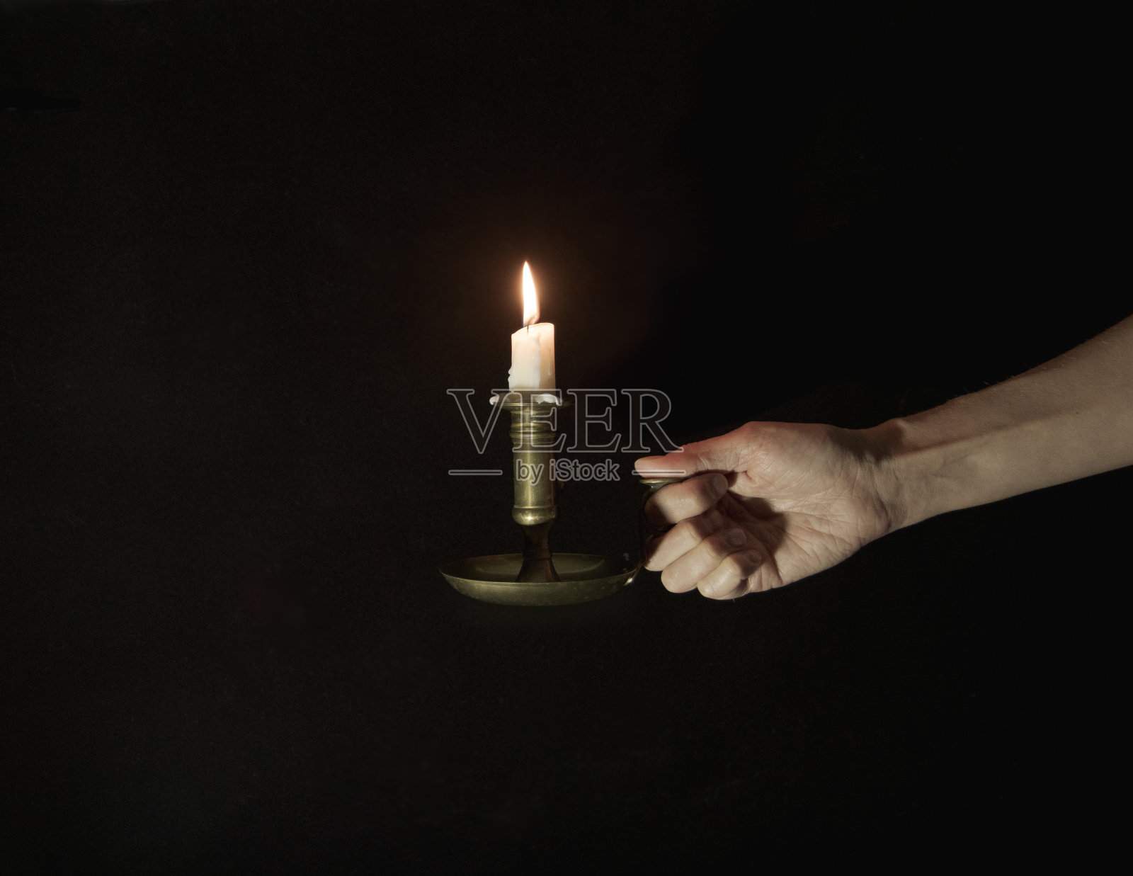 装饰铜烛台与燃烧的蜡烛在一个女性的手在黑色背景照片摄影图片