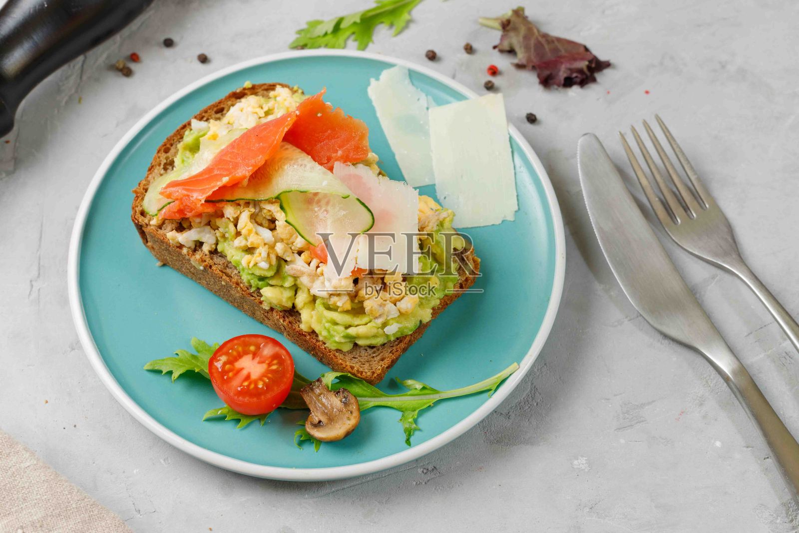 吐司配炒鸡蛋，鳄梨，烟熏鲑鱼和黑麦面包蔬菜。在蓝色的盘子上，水平的照片摄影图片