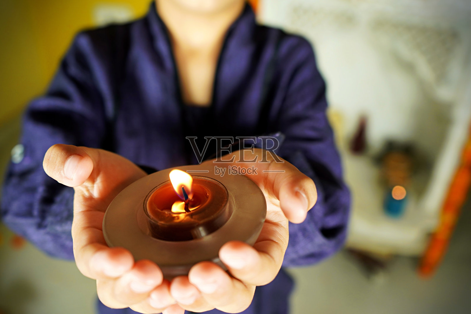 一个小孩双手合十，拿着一根点燃的平蜡烛照片摄影图片