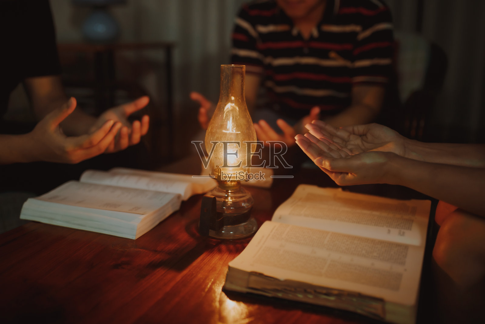 晚上，基督教家庭在家里的木桌上放着一盏老式灯，一起在模糊的圣经上祈祷照片摄影图片