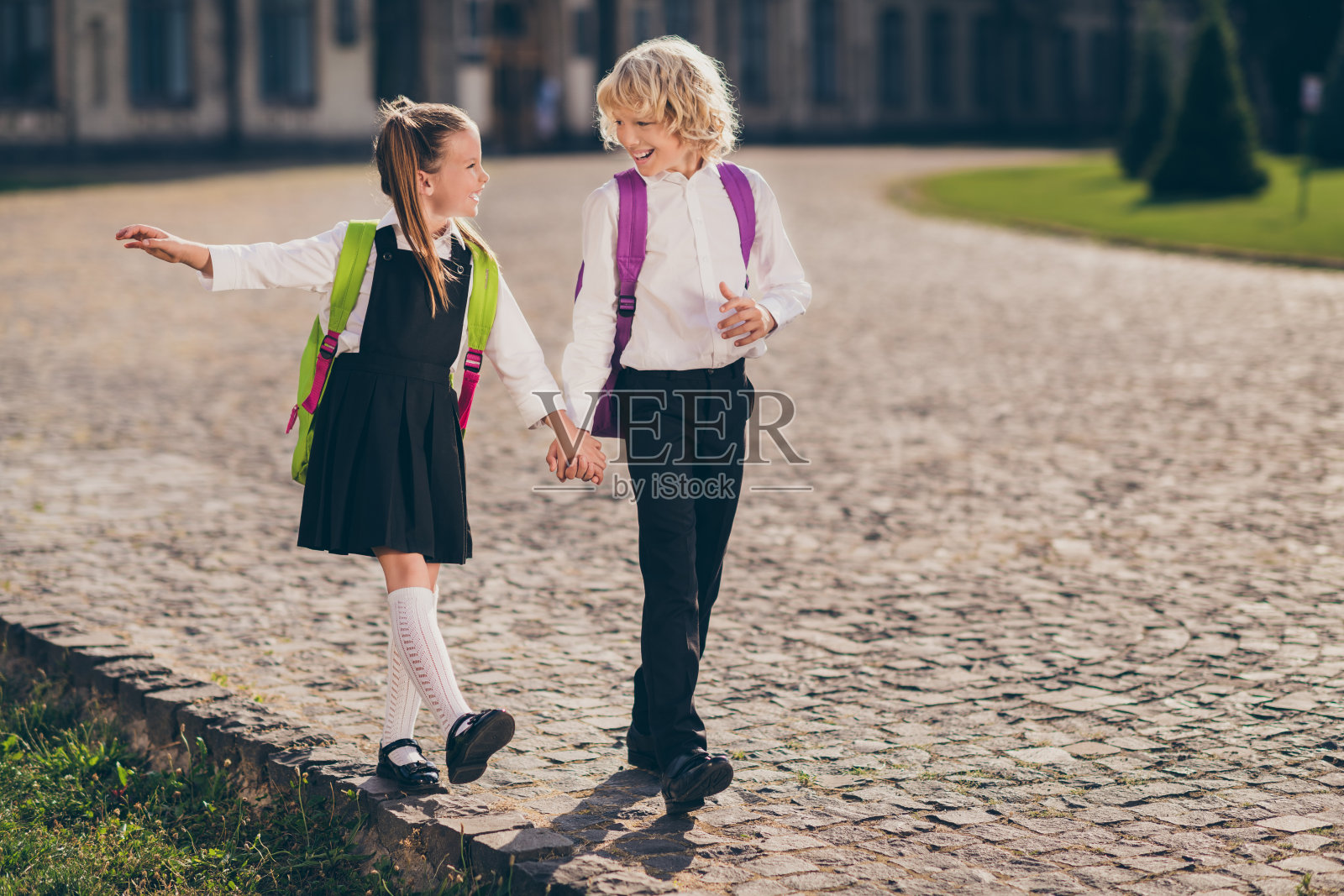 两人无忧无虑的照片，孩子们手牵着手享受散步，穿书包，校服在街道外面照片摄影图片